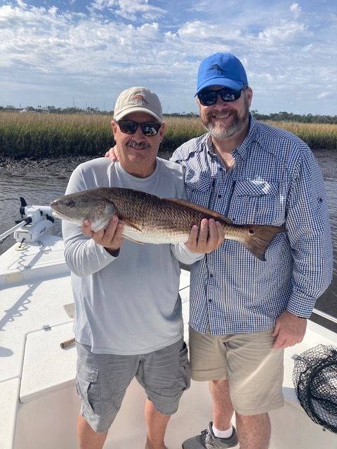 Two men are standing on a boat holding a large fish.