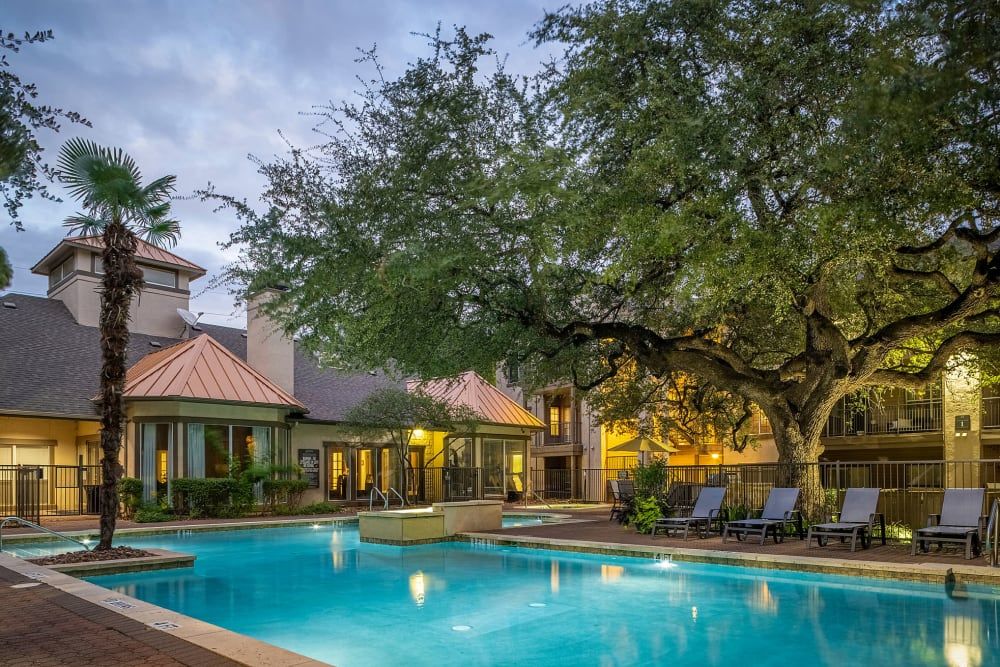 a large swimming pool is surrounded by chairs and trees in front of a building at Marquis at Ladera Vista in Austin, TX.