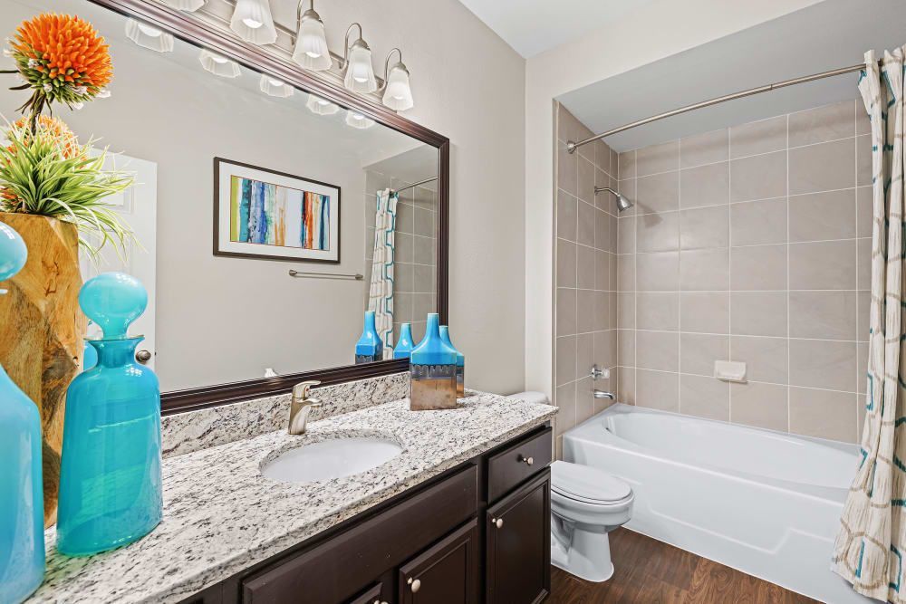 a bathroom with a sink, toilet, tub, and mirror at Marquis at Ladera Vista in Austin, TX.