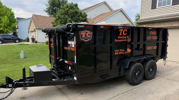 A dumpster trailer is parked in a parking lot in front of a brick building.