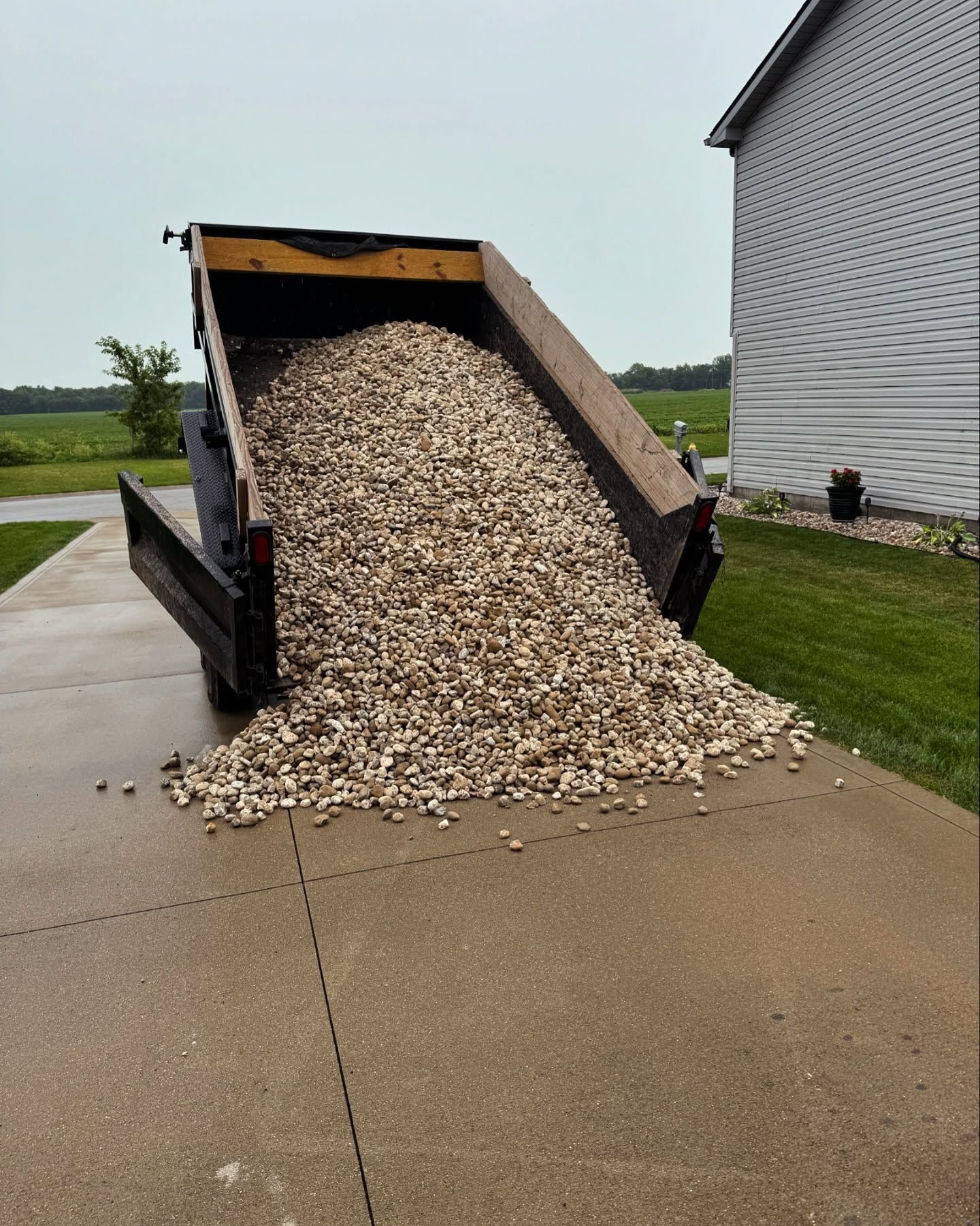 A dumpster filled with gravel is sitting on a sidewalk in front of a house.