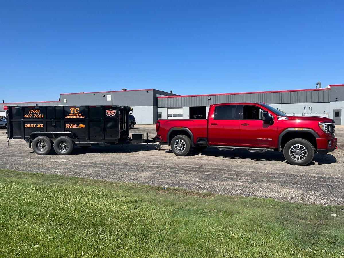 A red truck is towing a dumpster on a trailer.