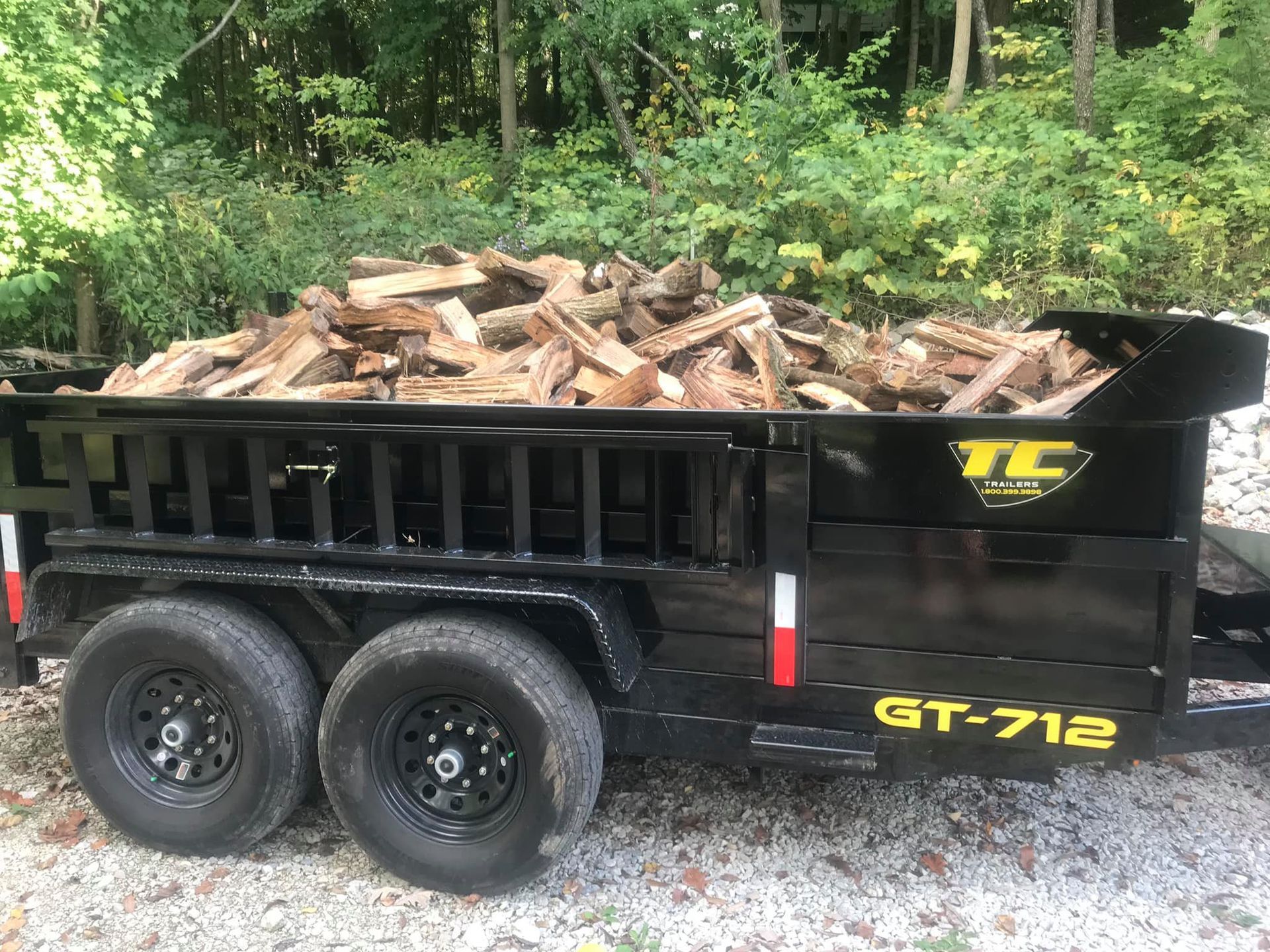A dump trailer filled with wood is parked in a gravel lot.