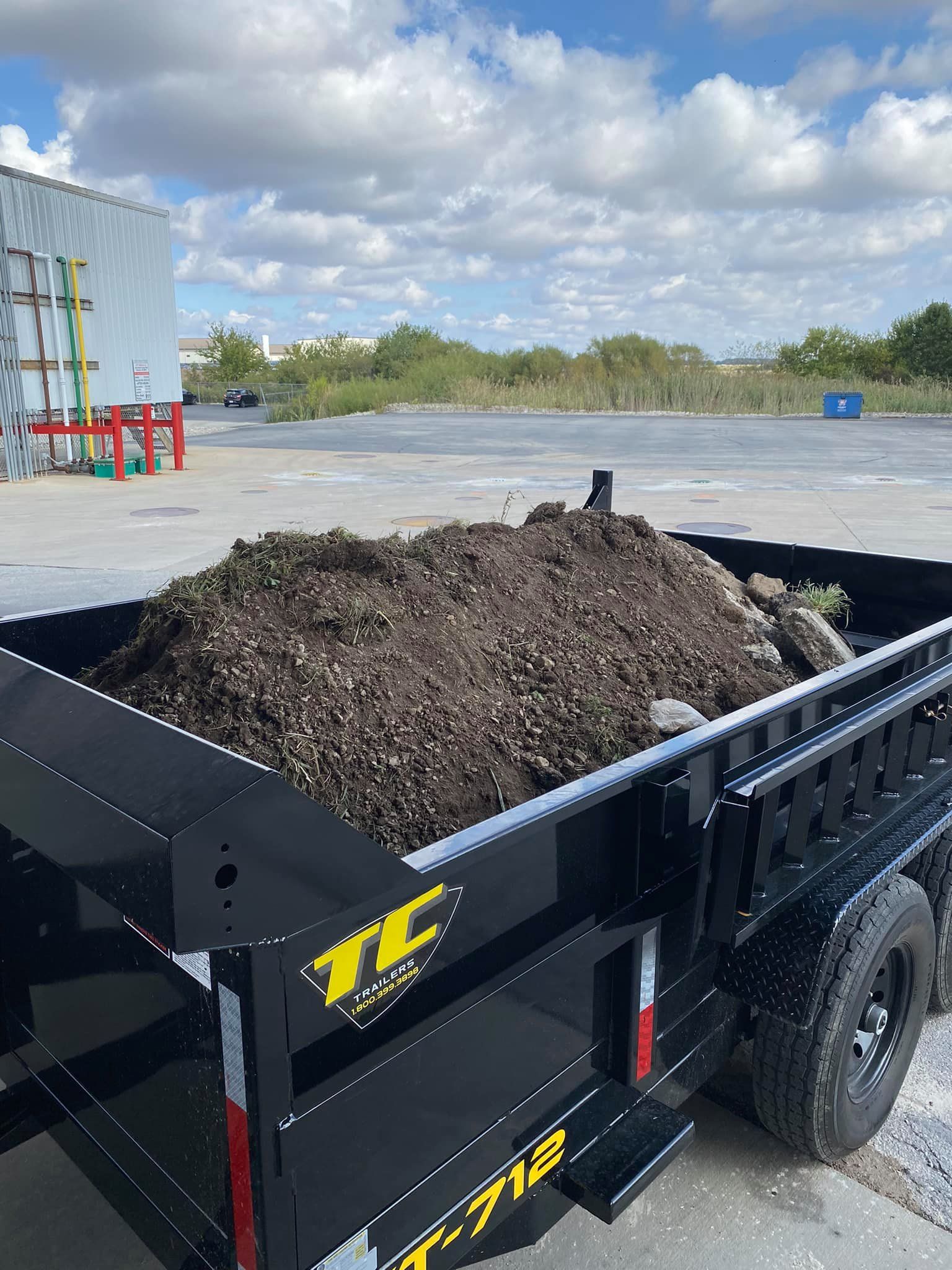 A dump trailer filled with dirt is parked in a parking lot.