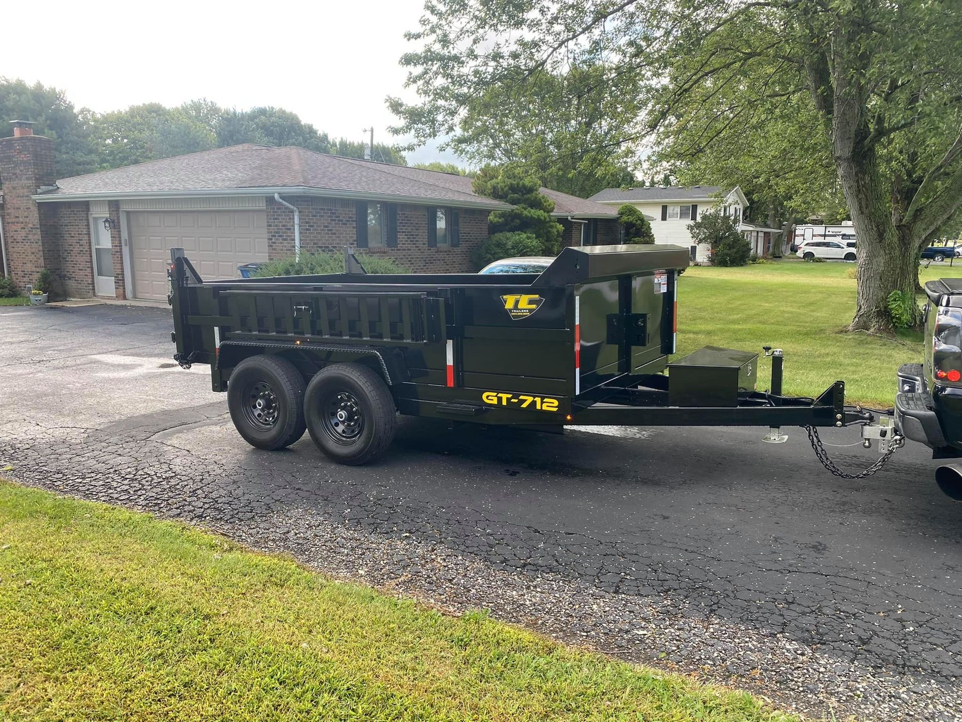 A dump trailer is parked on the side of the road next to a house.