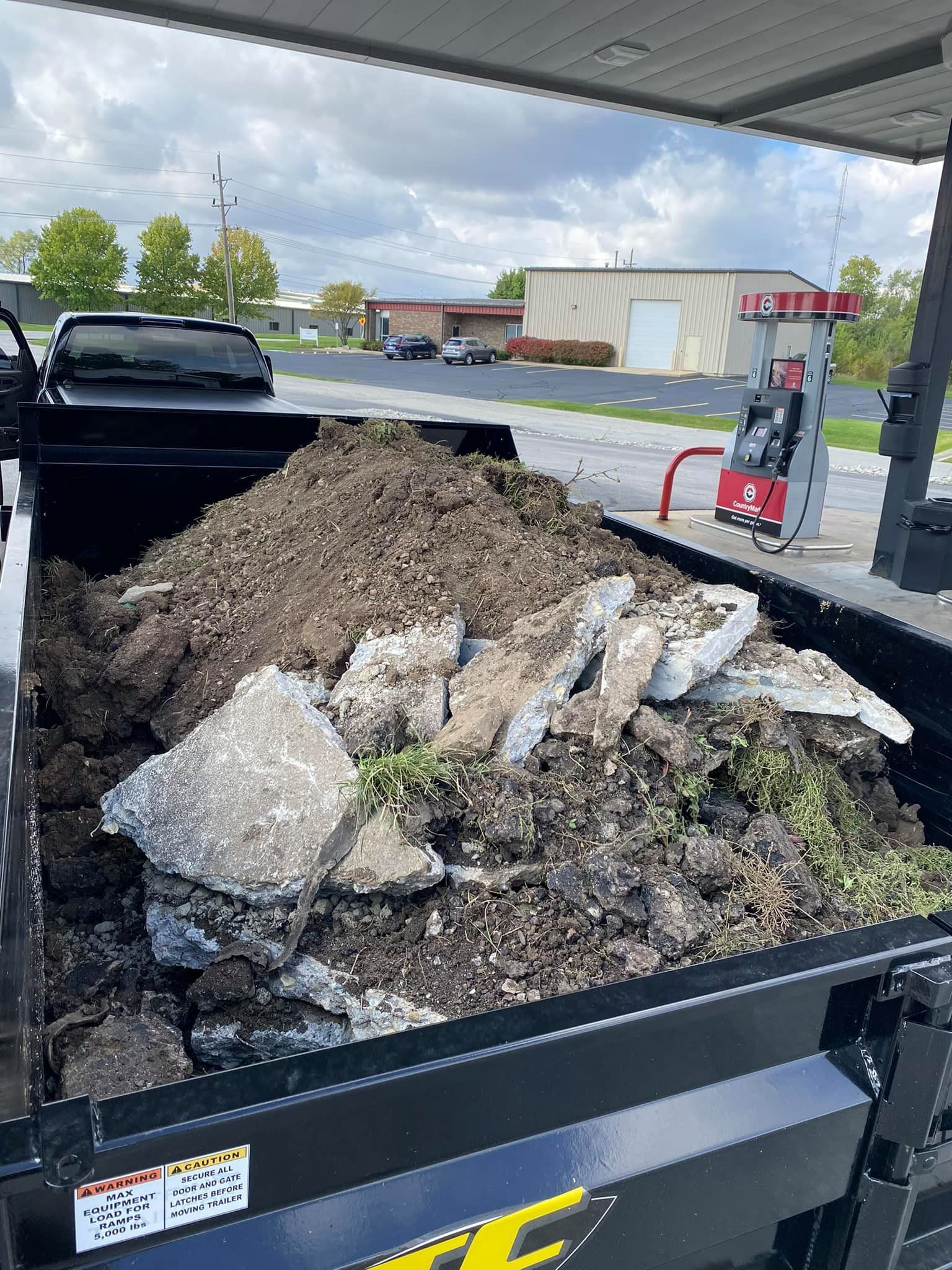 A dumpster filled with rocks and dirt is parked at a gas station.