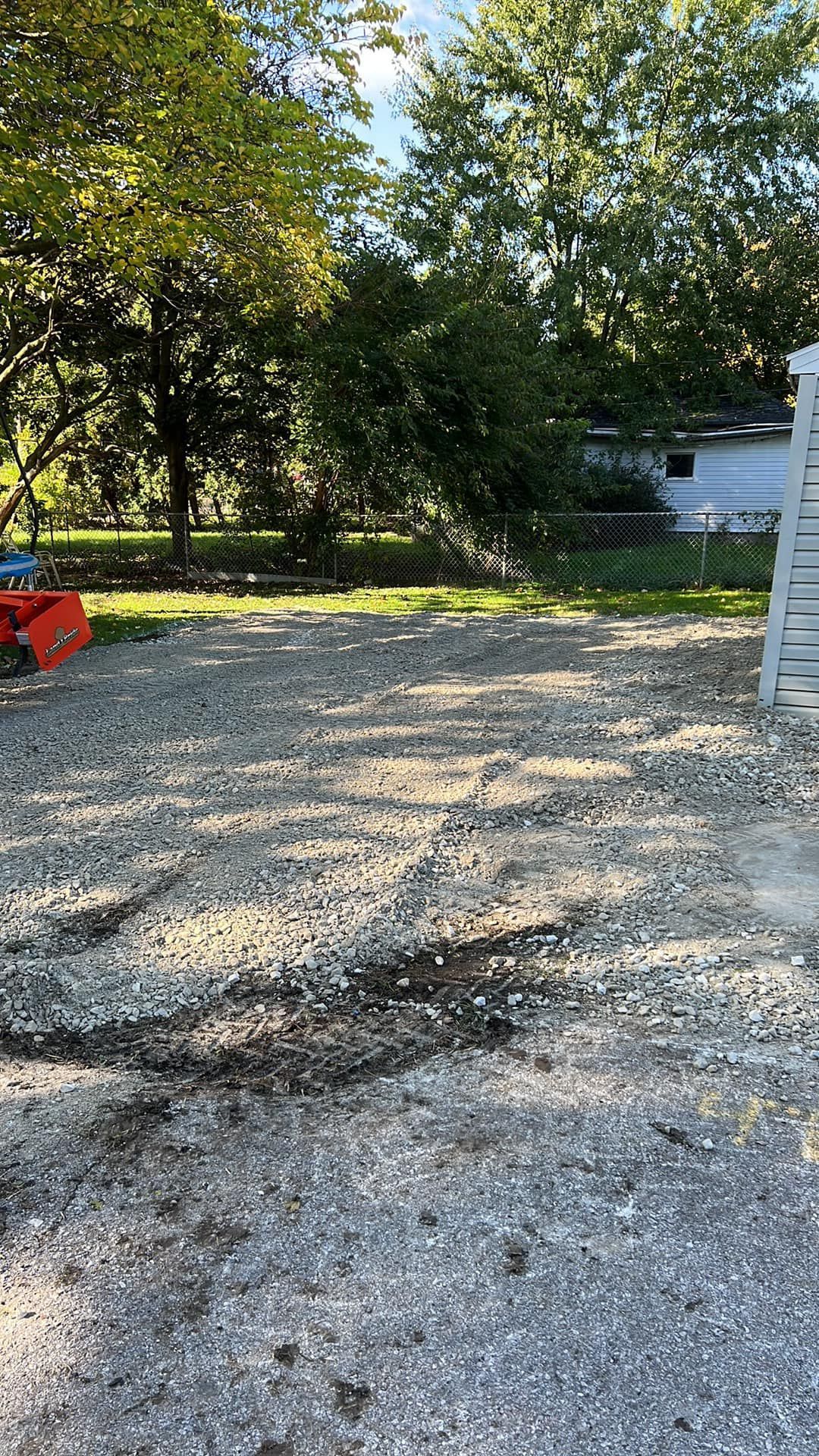 A gravel driveway with a shed and trees in the background.