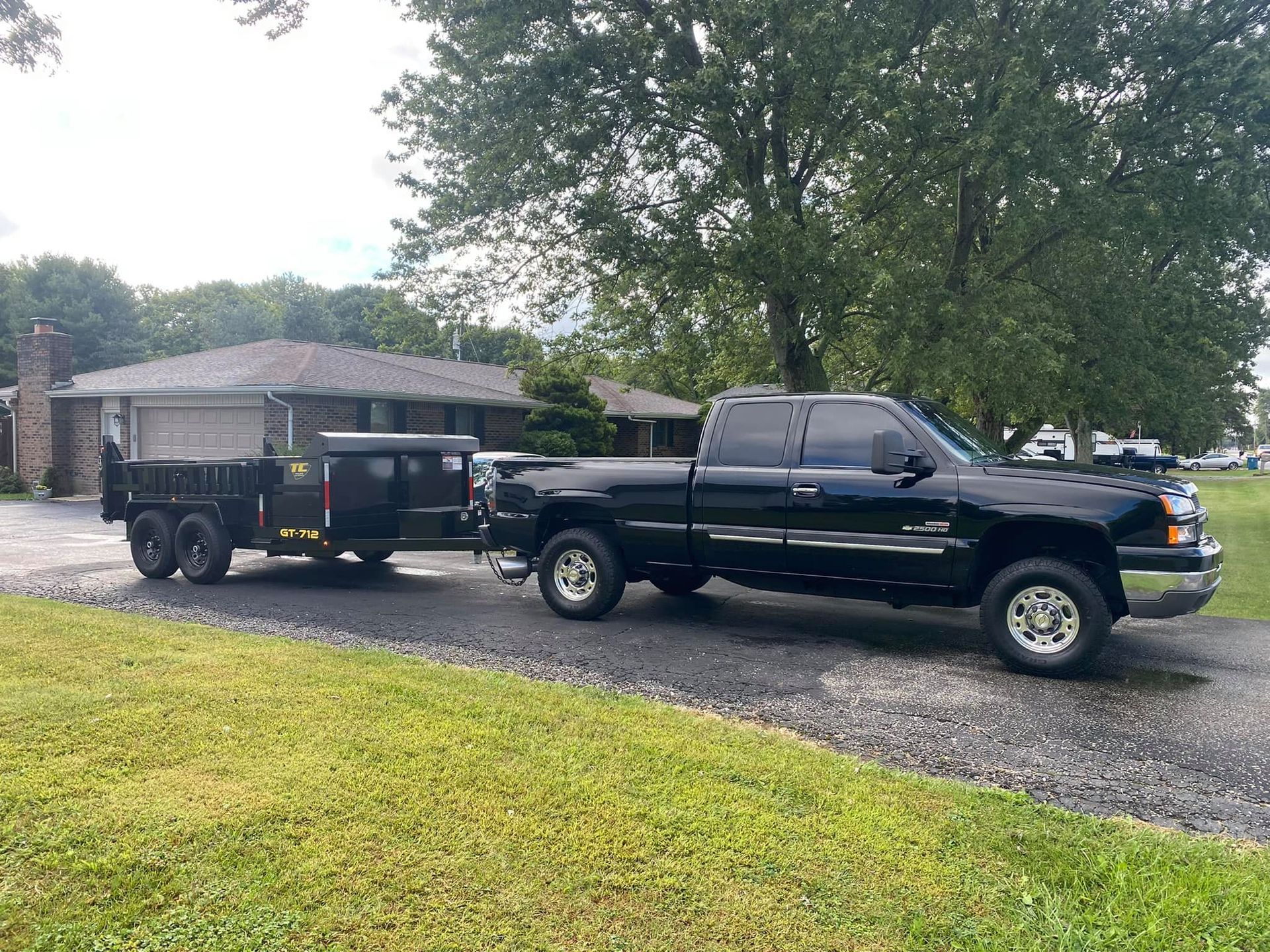A black truck with a trailer attached to it is parked in front of a house.