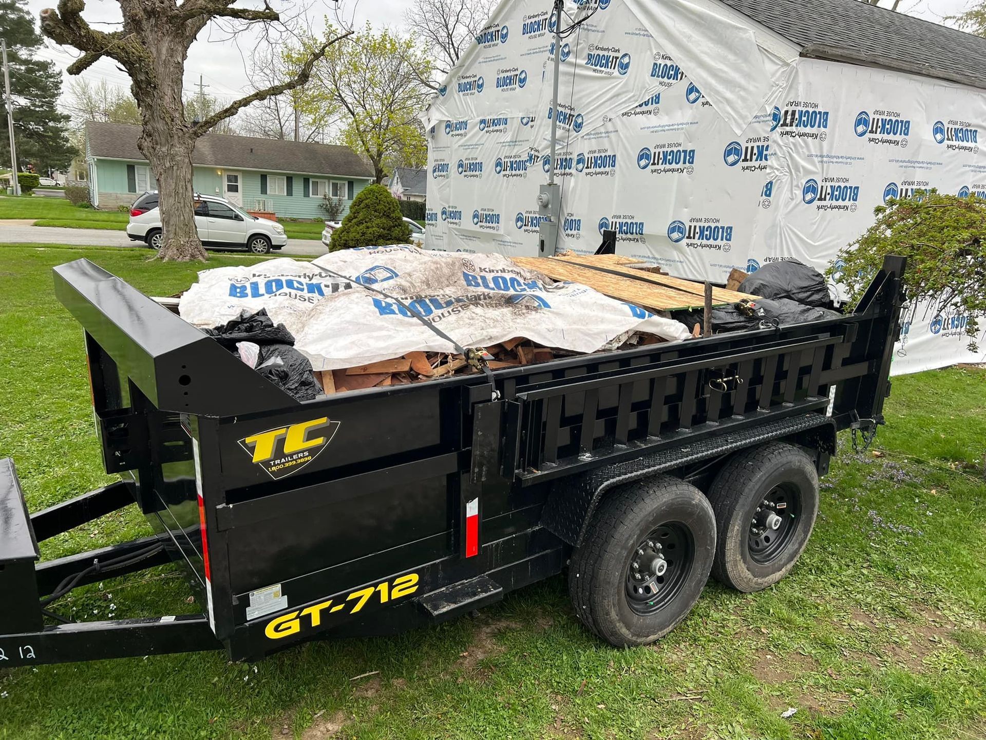 A dumpster trailer is parked in the grass in front of a house.
