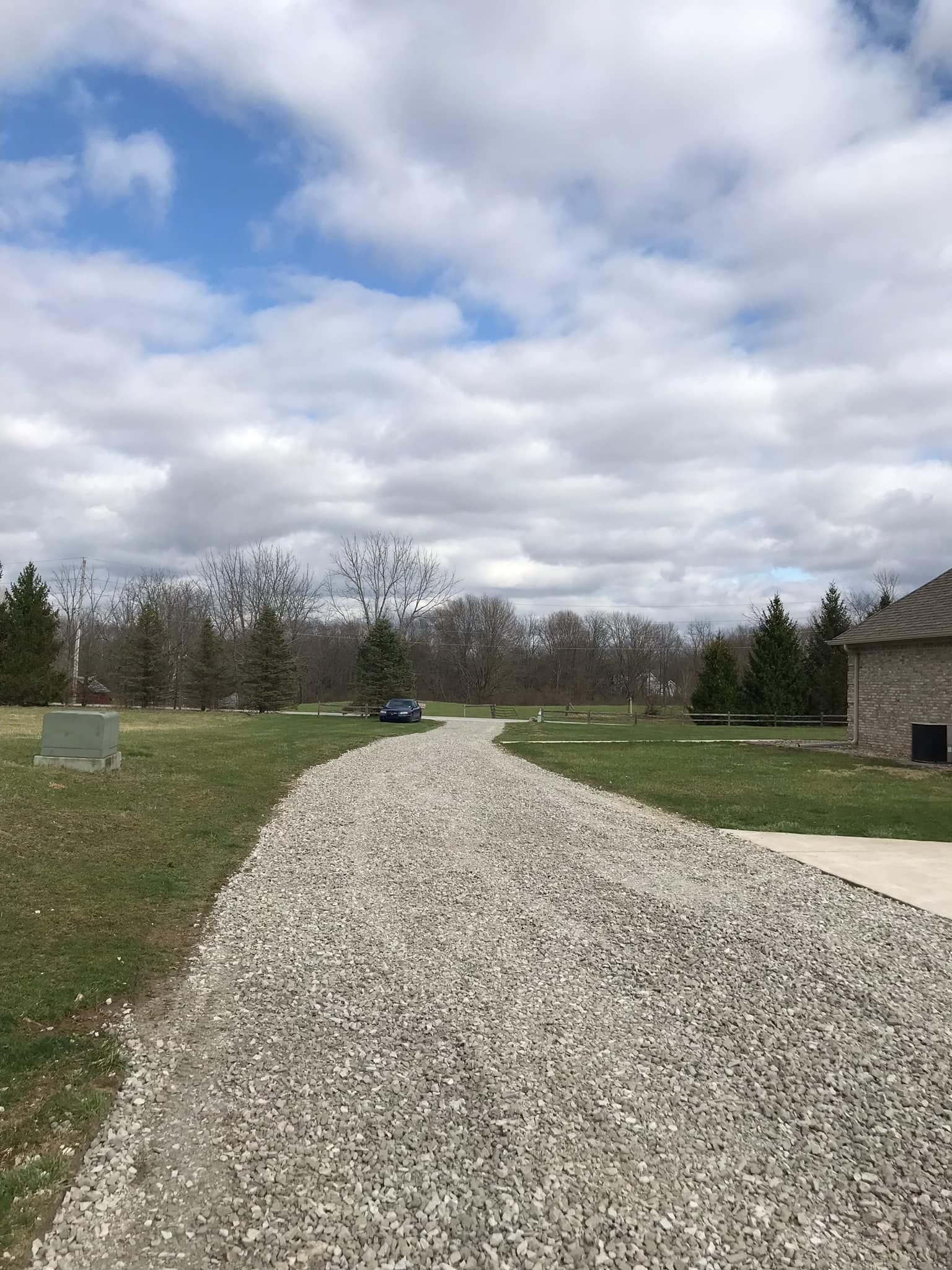 A gravel driveway leading to a house in the middle of a grassy field.