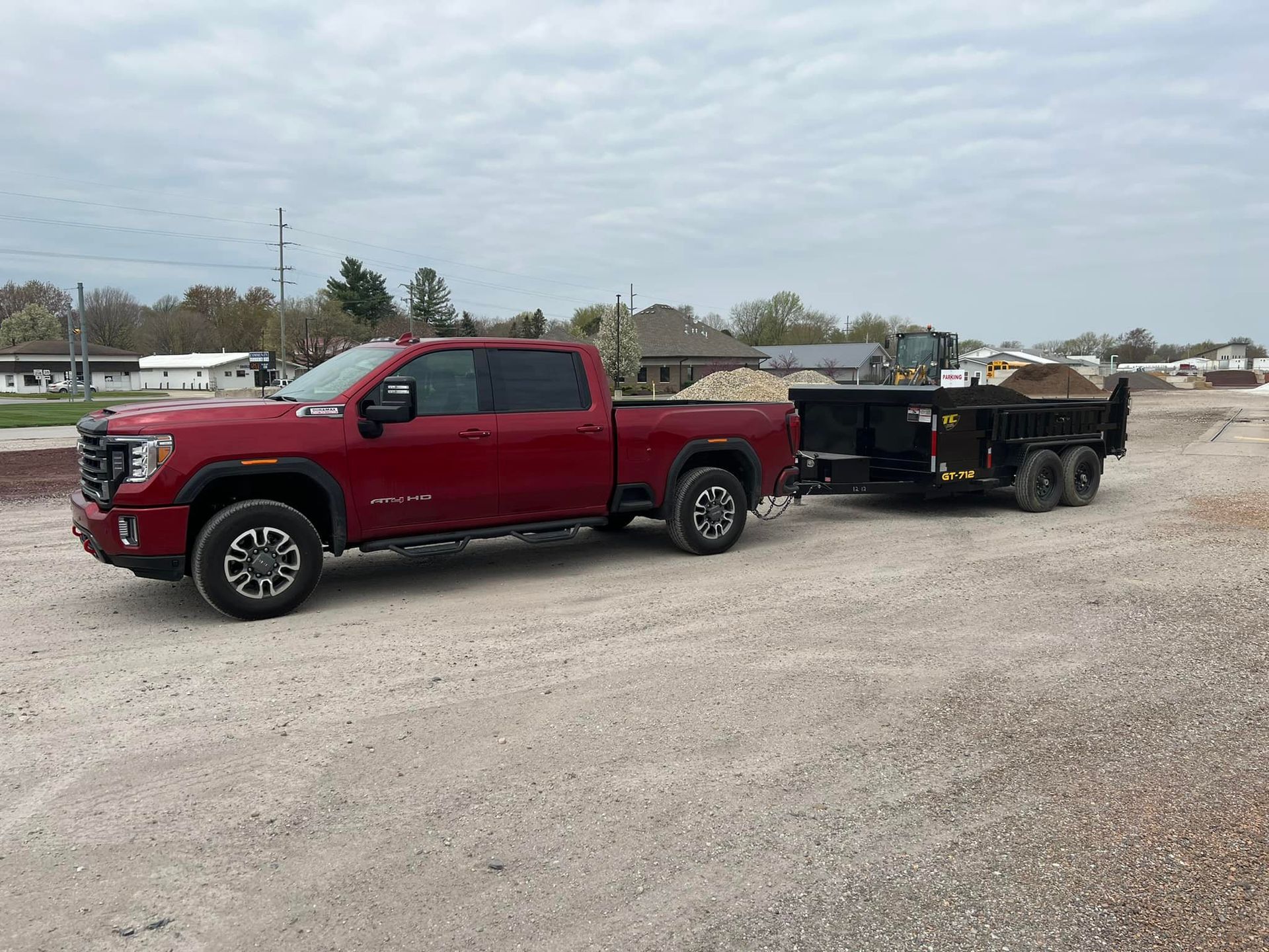 A red truck is towing a dump truck in a gravel lot.