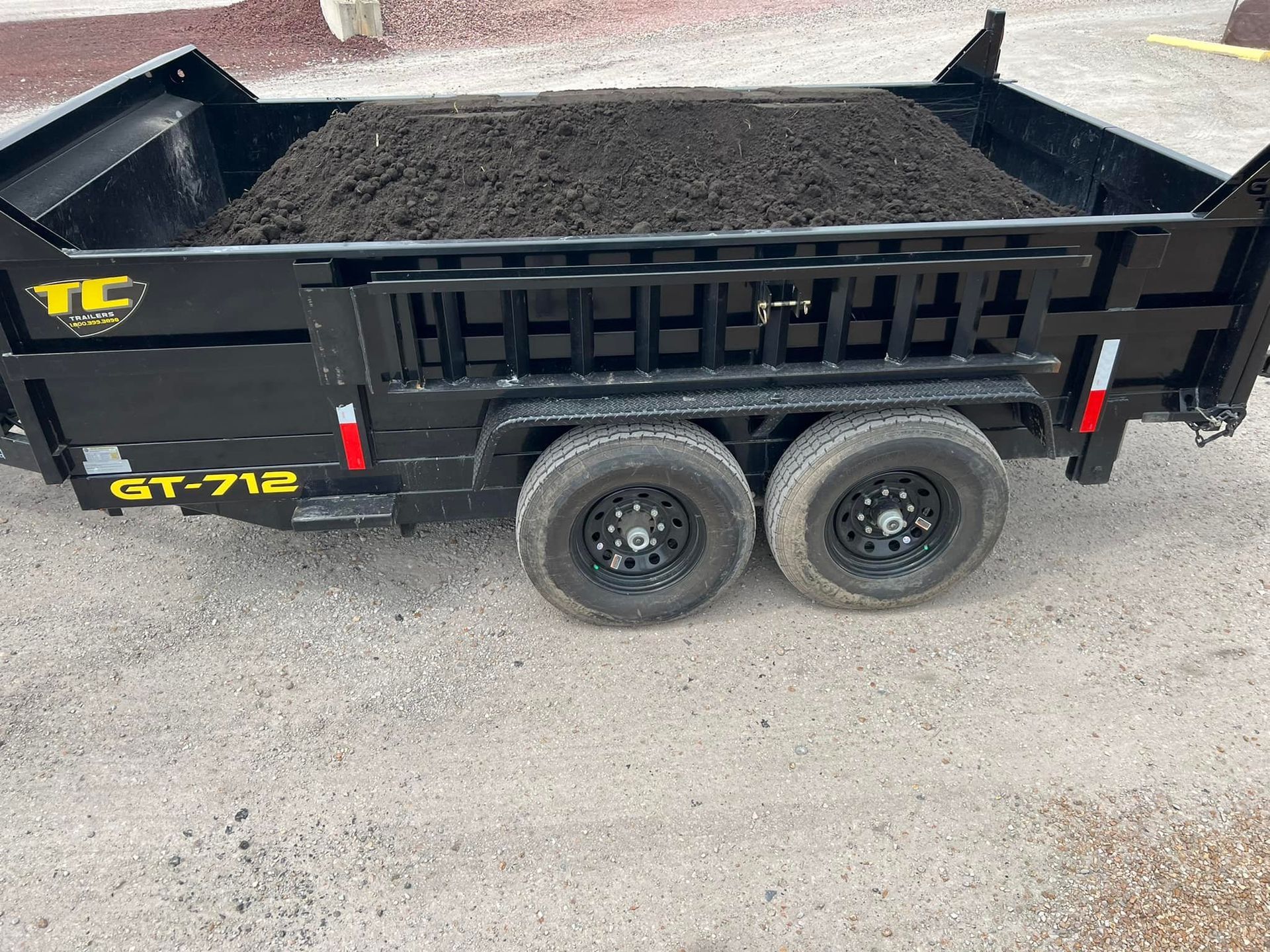 A dump trailer filled with dirt is parked on the side of the road.