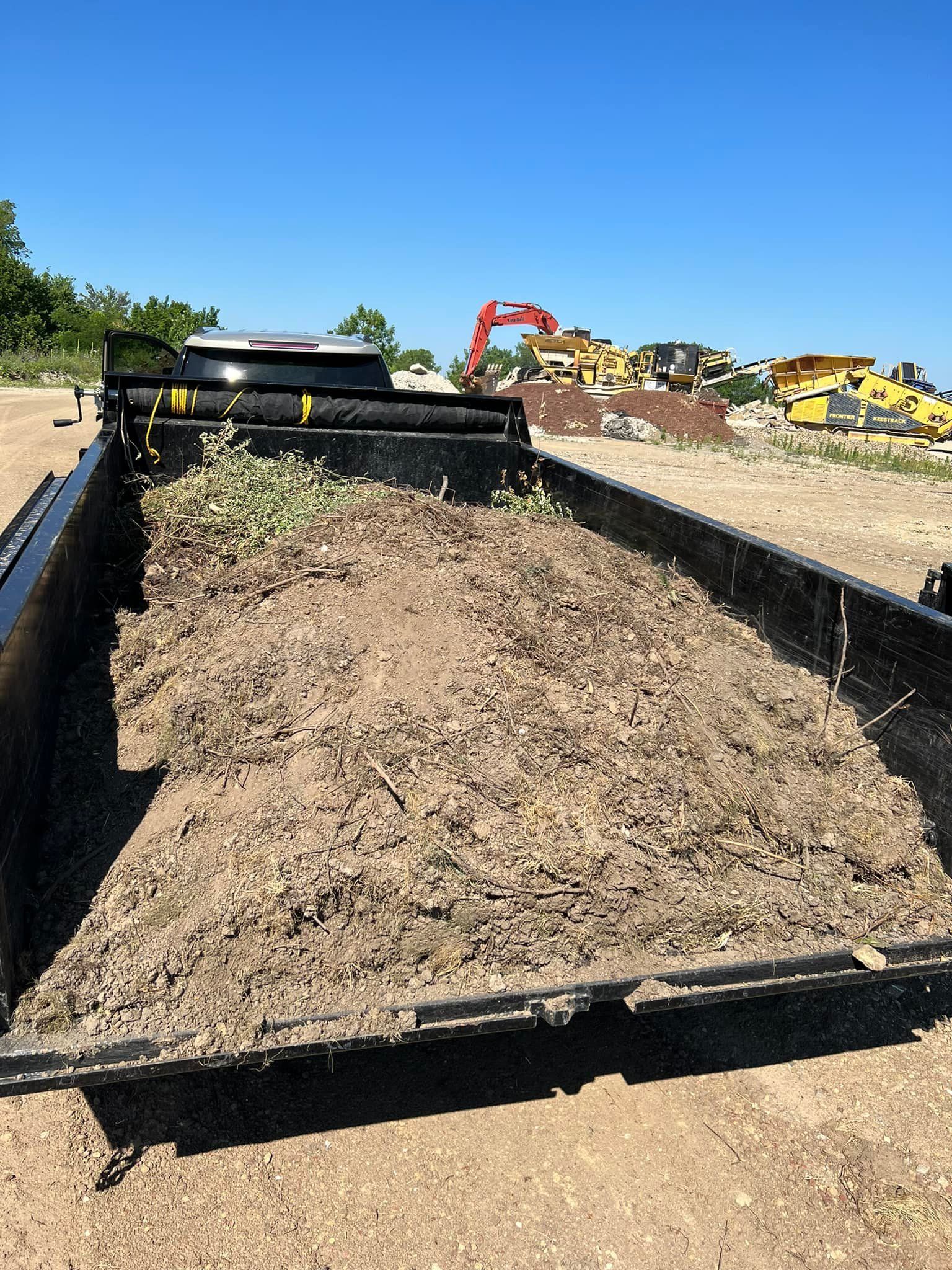 A truck with a trailer full of dirt is parked in a field.