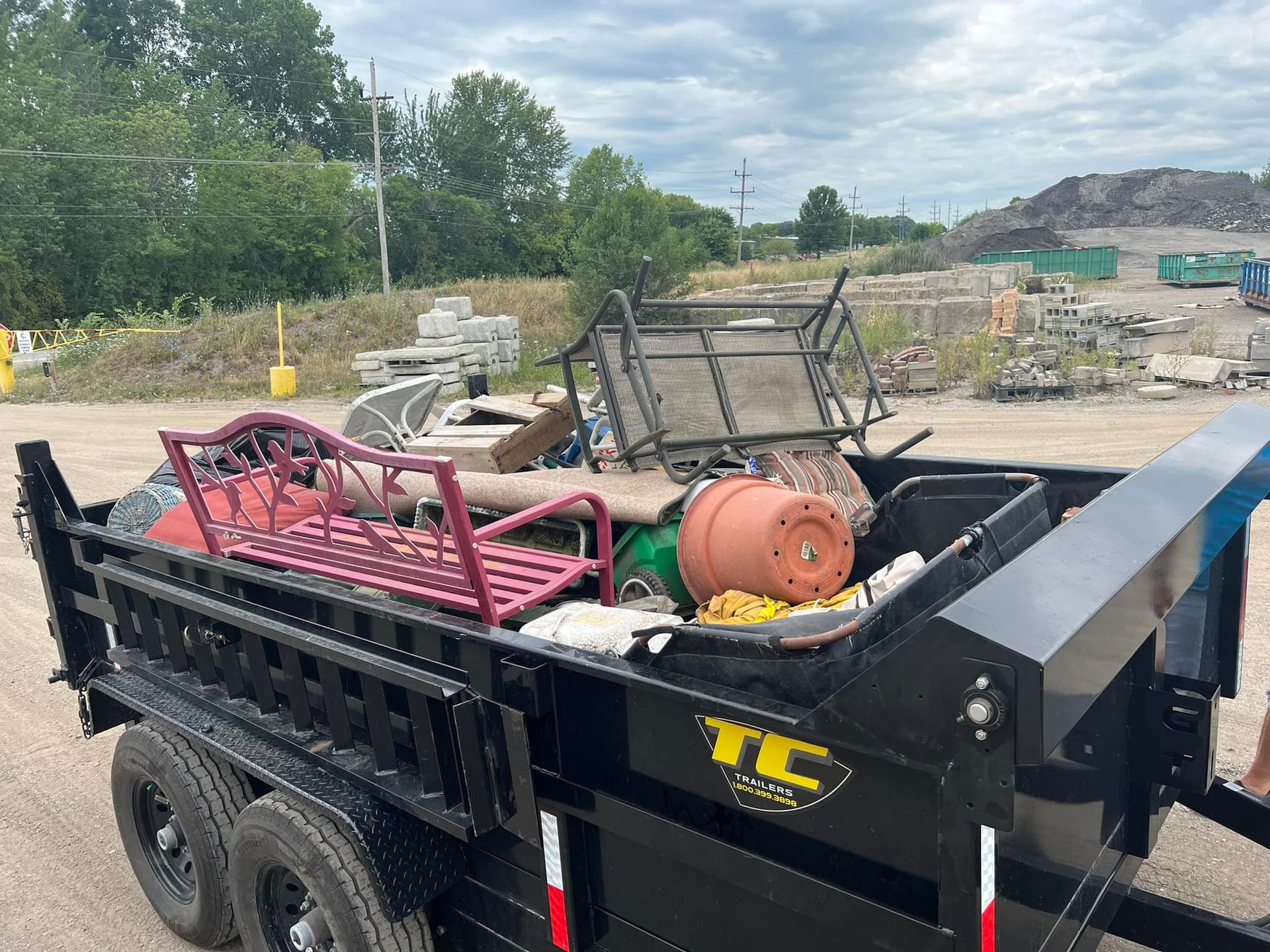A dumpster trailer filled with junk is parked in a dirt lot.