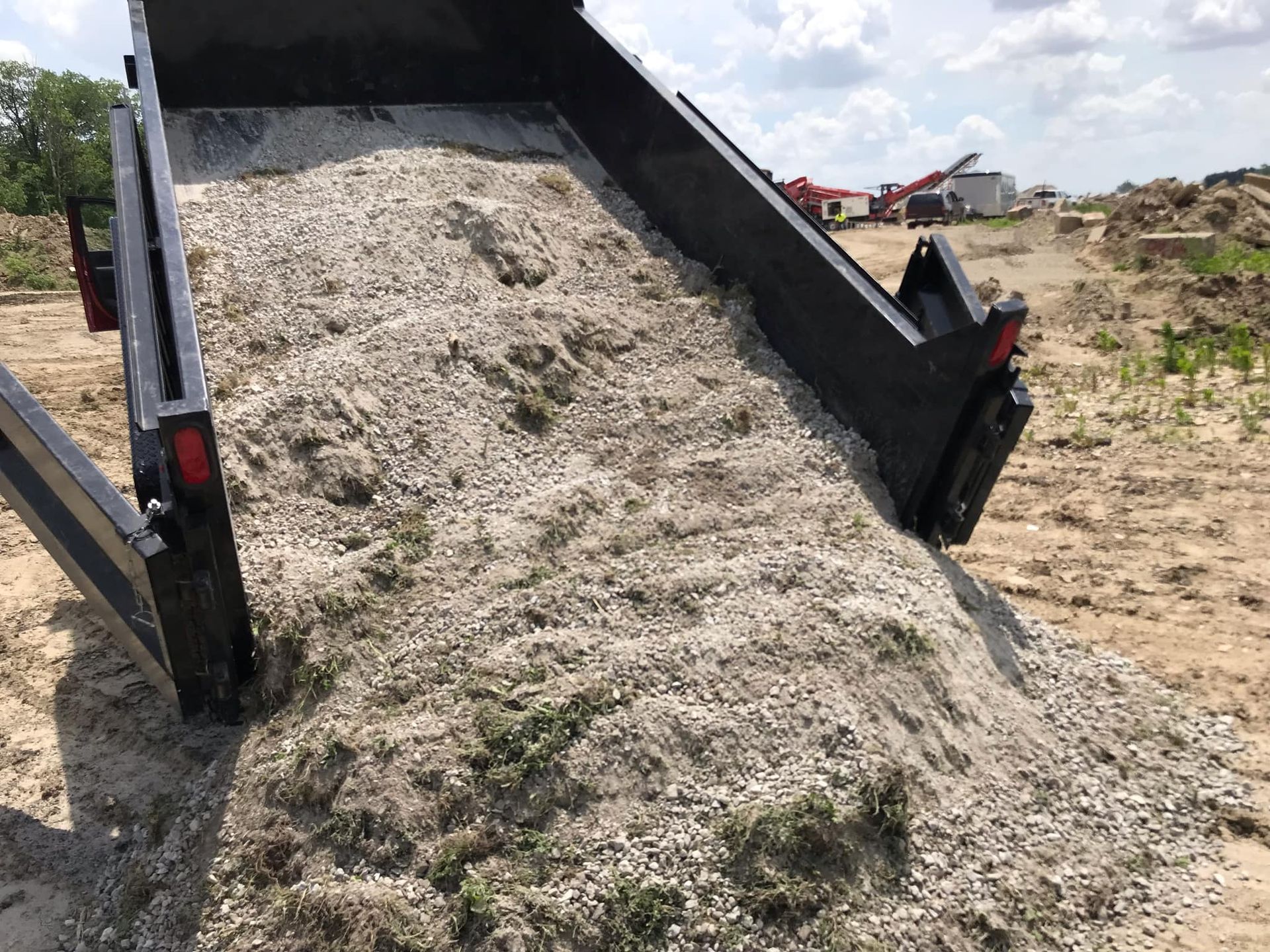 A dumpster filled with gravel is sitting on top of a dirt field.