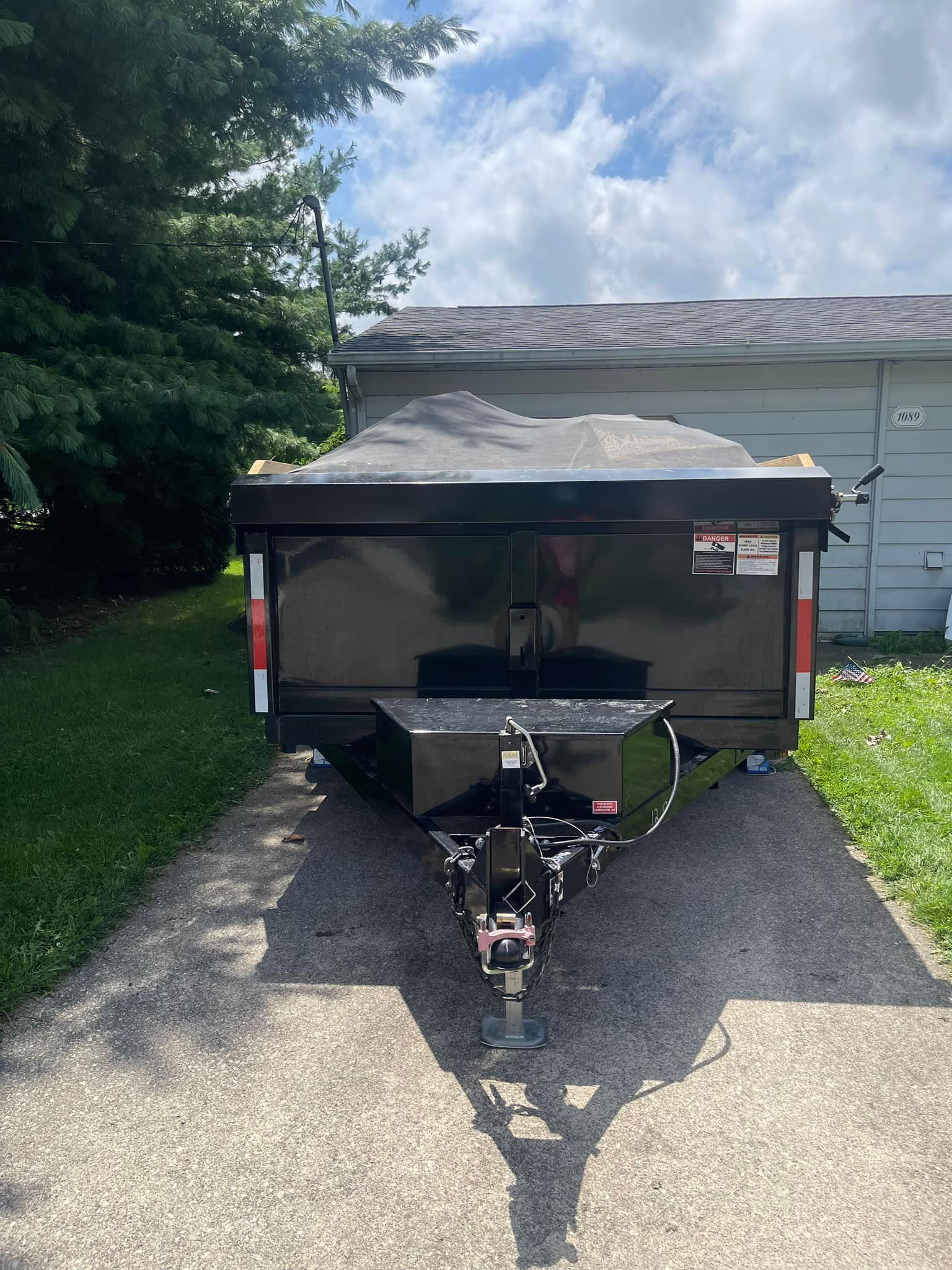 A dumpster trailer is parked in a driveway next to a garage.
