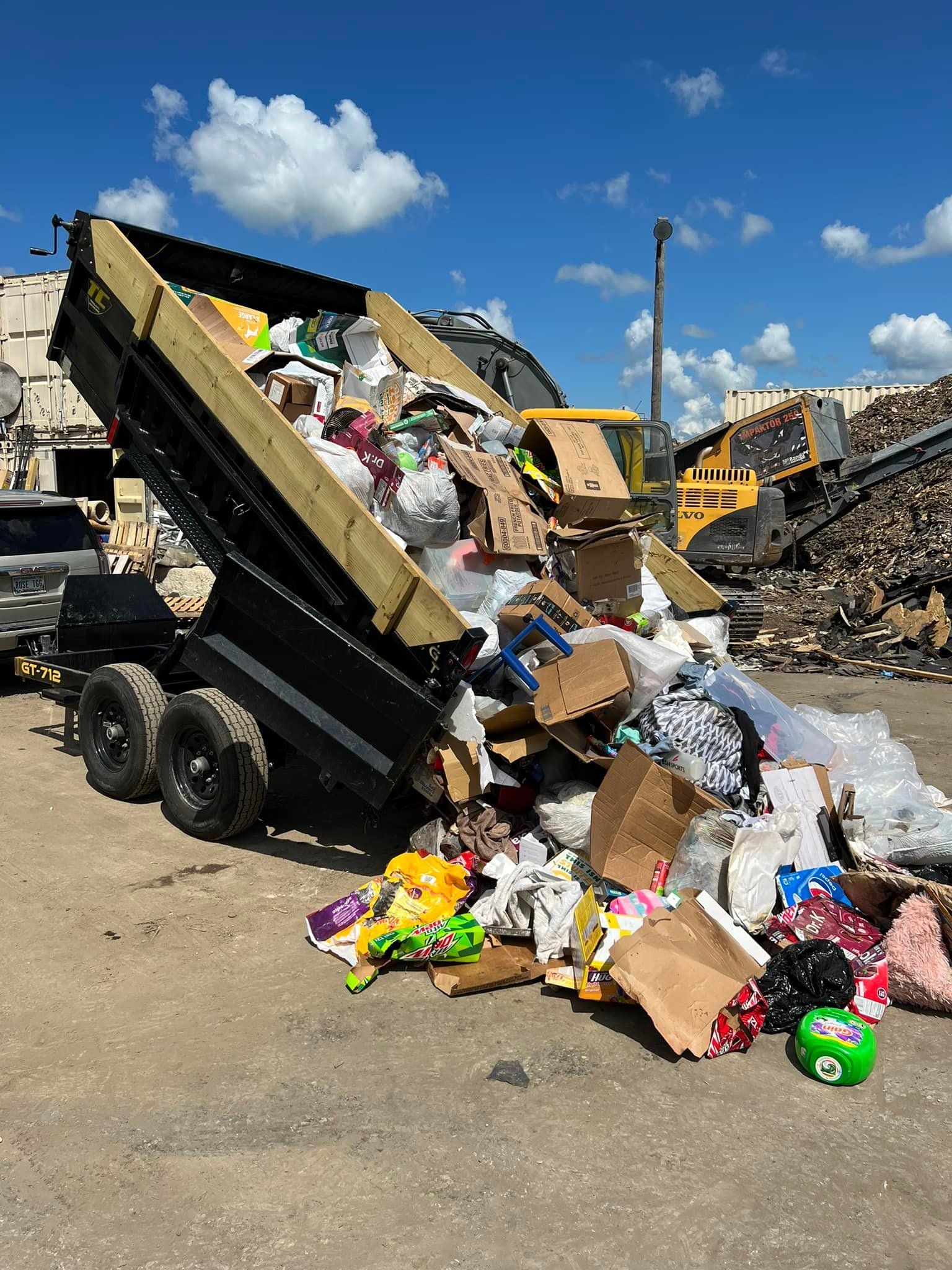 A dump truck is loading a large pile of trash into a trailer.