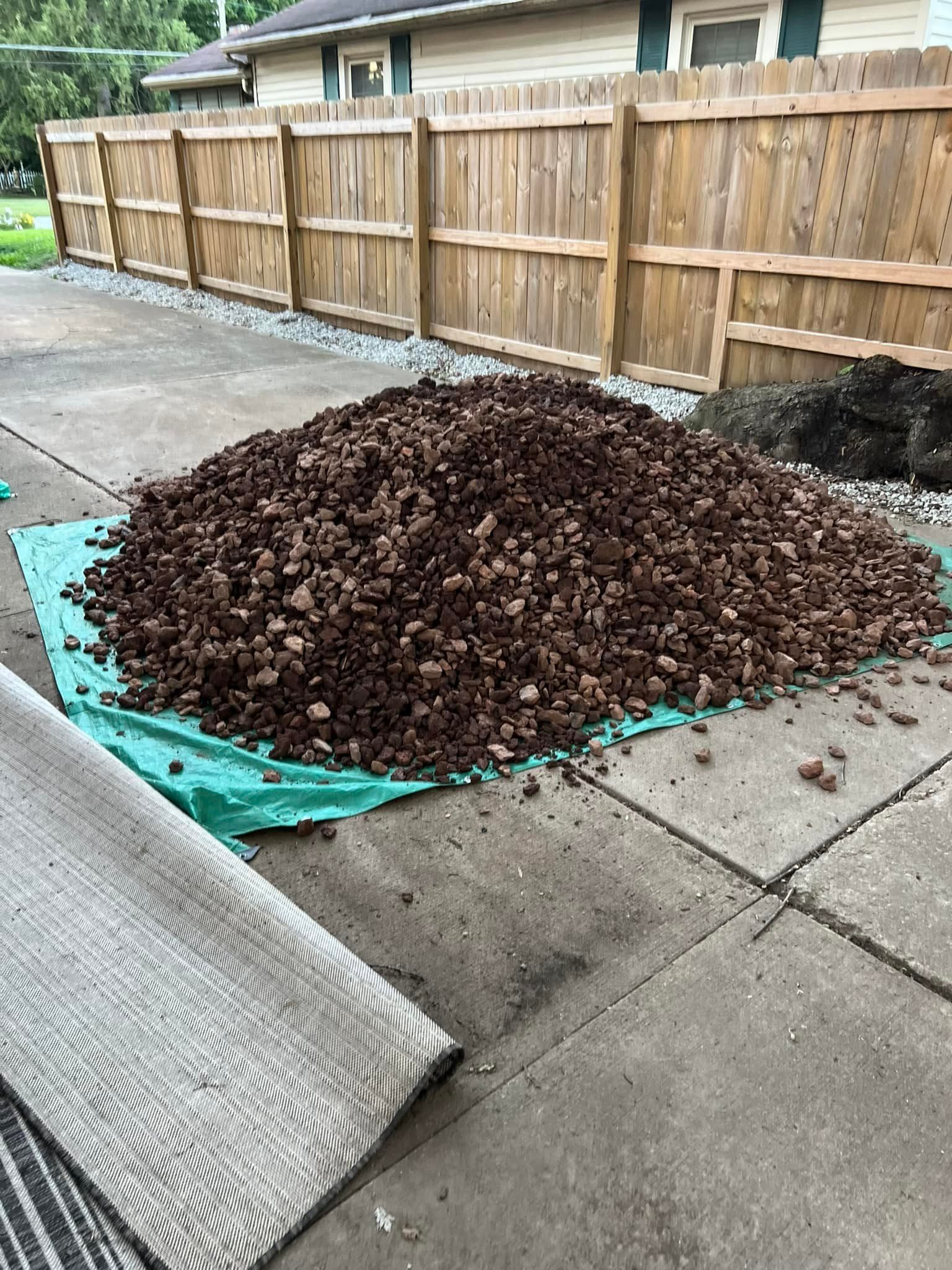 A pile of mulch is sitting on the sidewalk next to a wooden fence.
