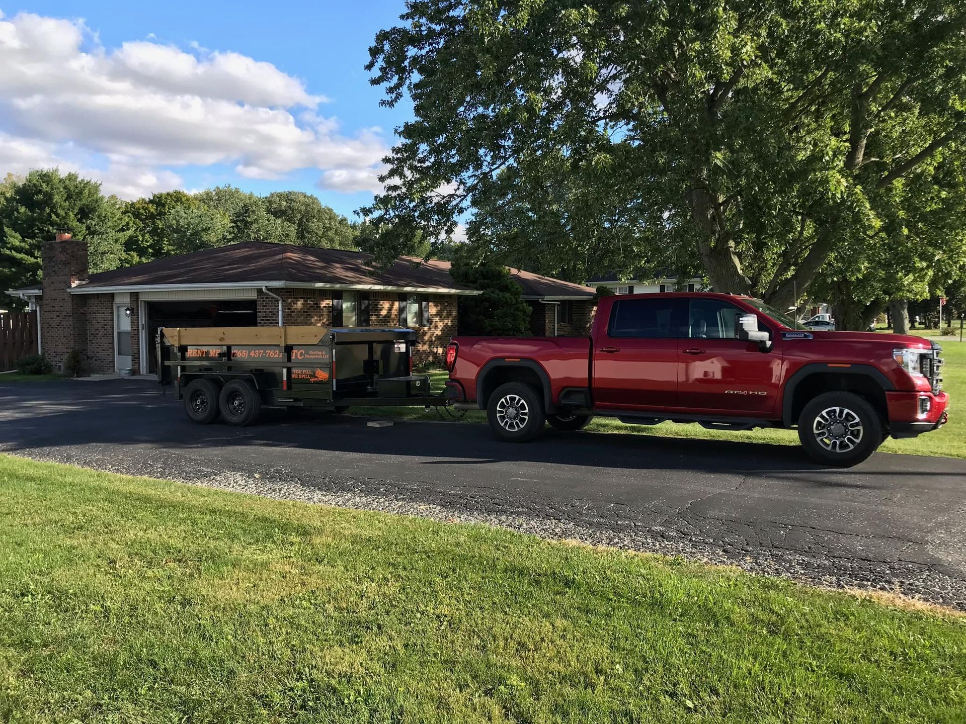 A red truck is towing a trailer in front of a house.