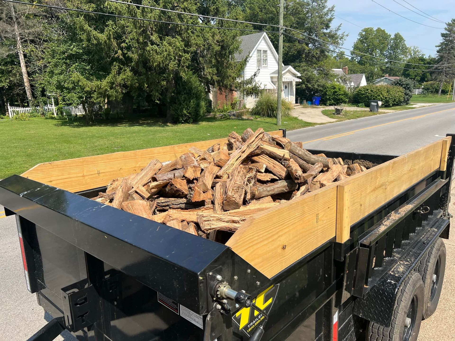 A dumpster filled with logs is parked on the side of the road.