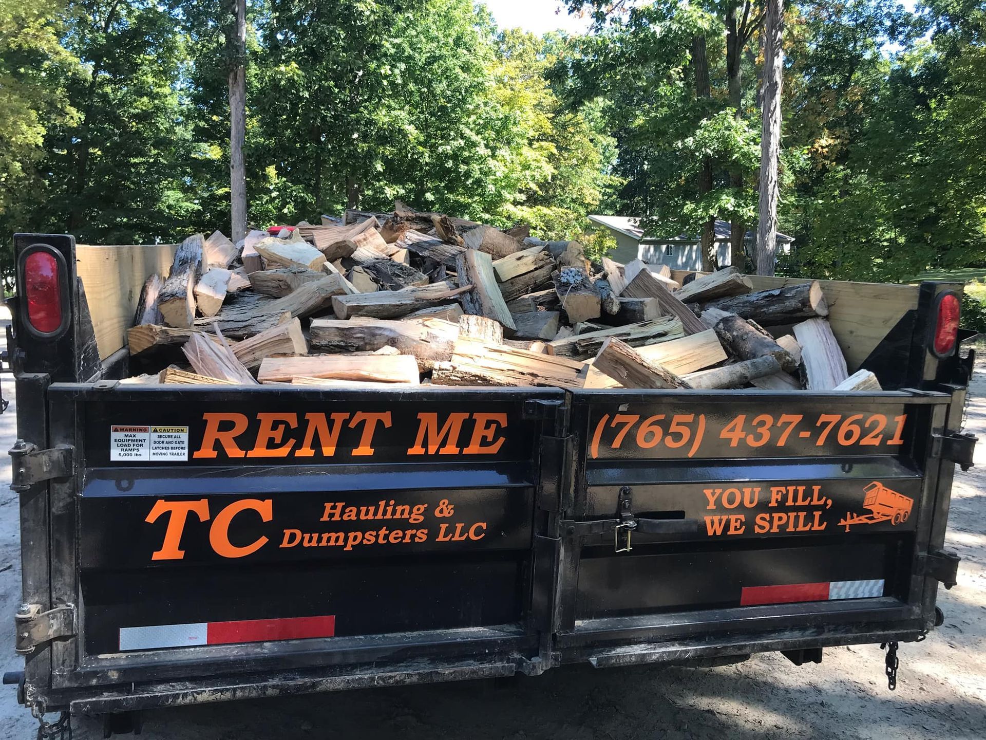 A dumpster filled with logs is parked on the side of the road.