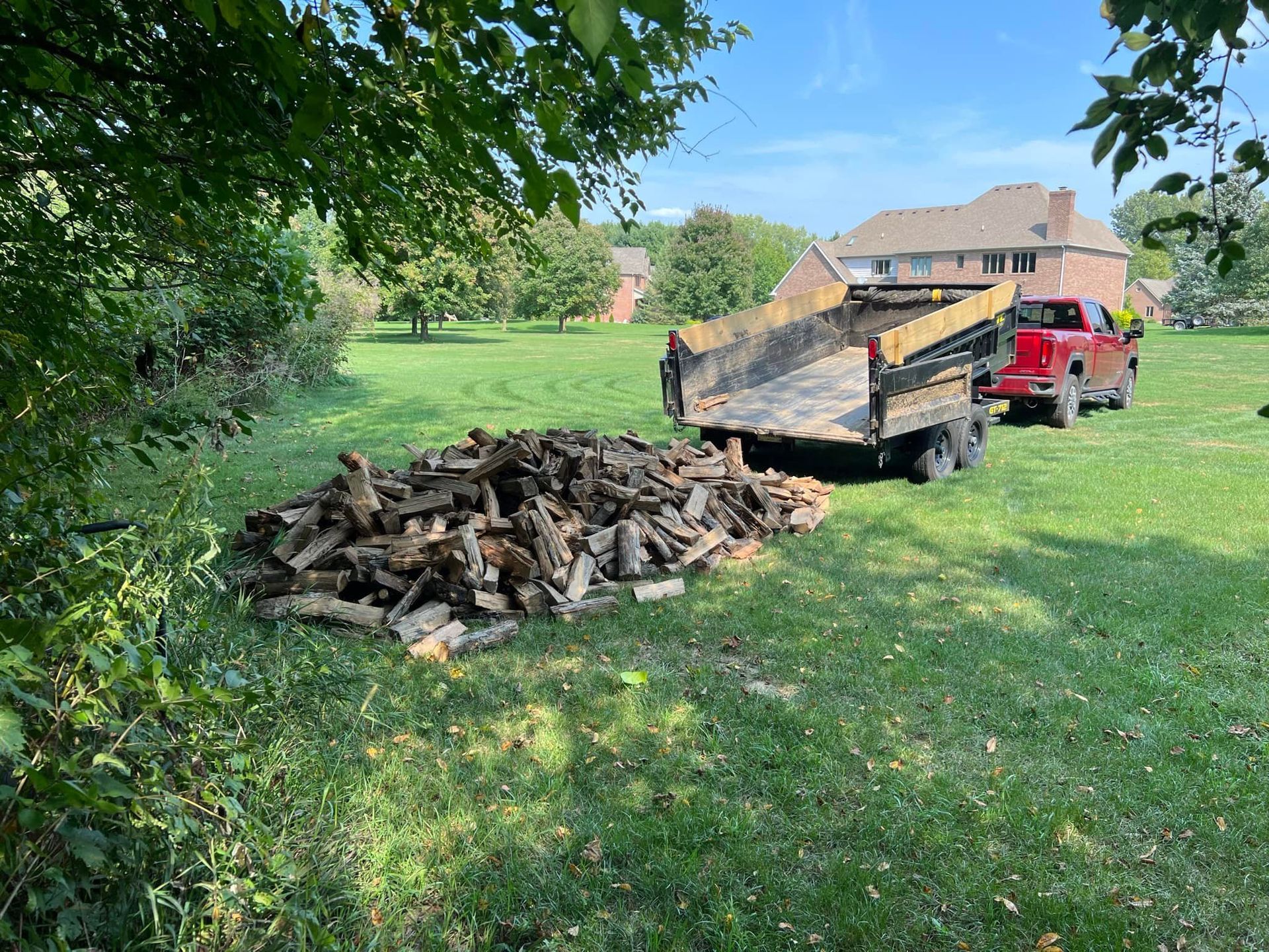 A red truck is towing a trailer full of logs in a grassy field.