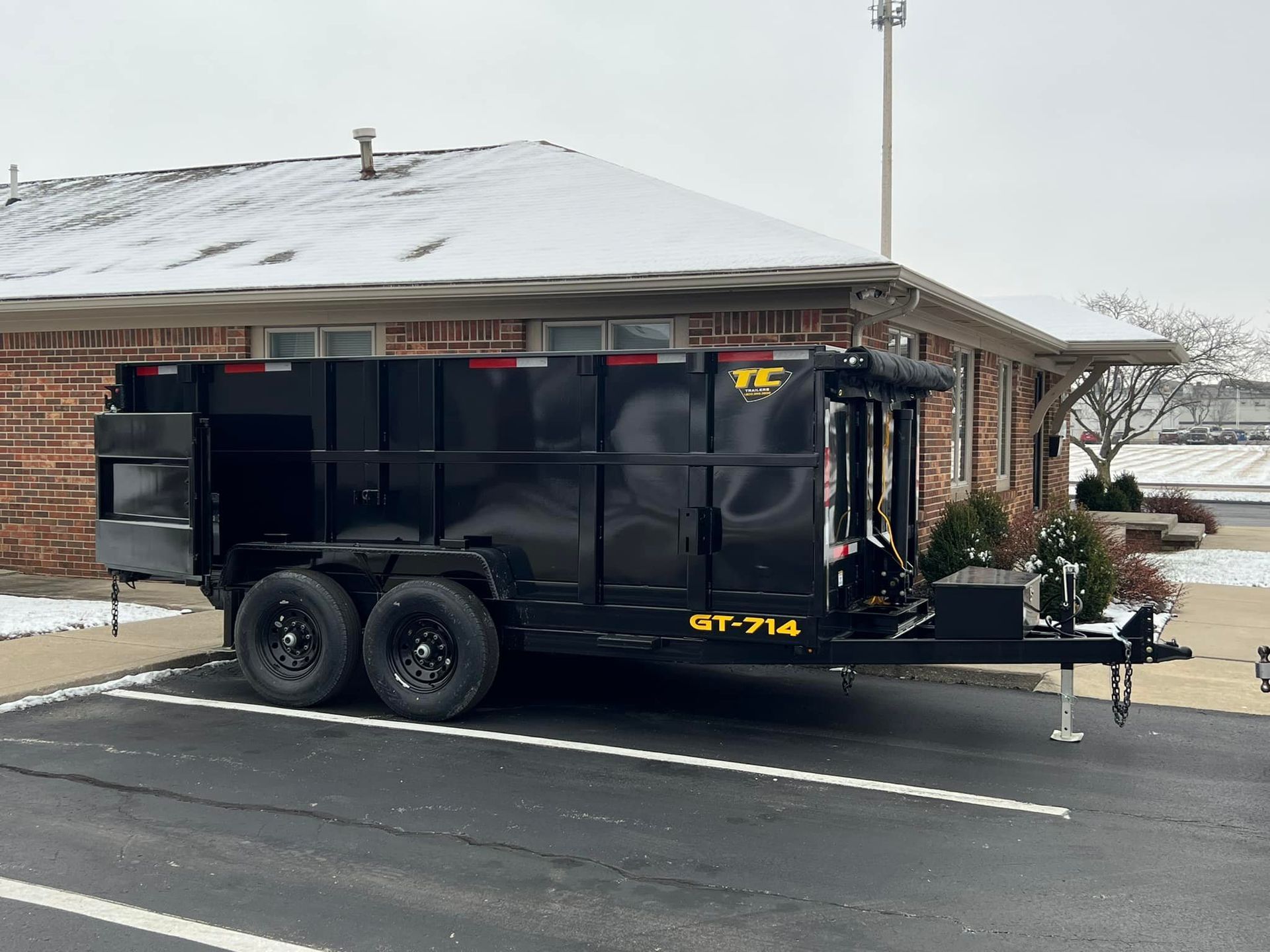 A dumpster trailer is parked in a parking lot in front of a brick building.