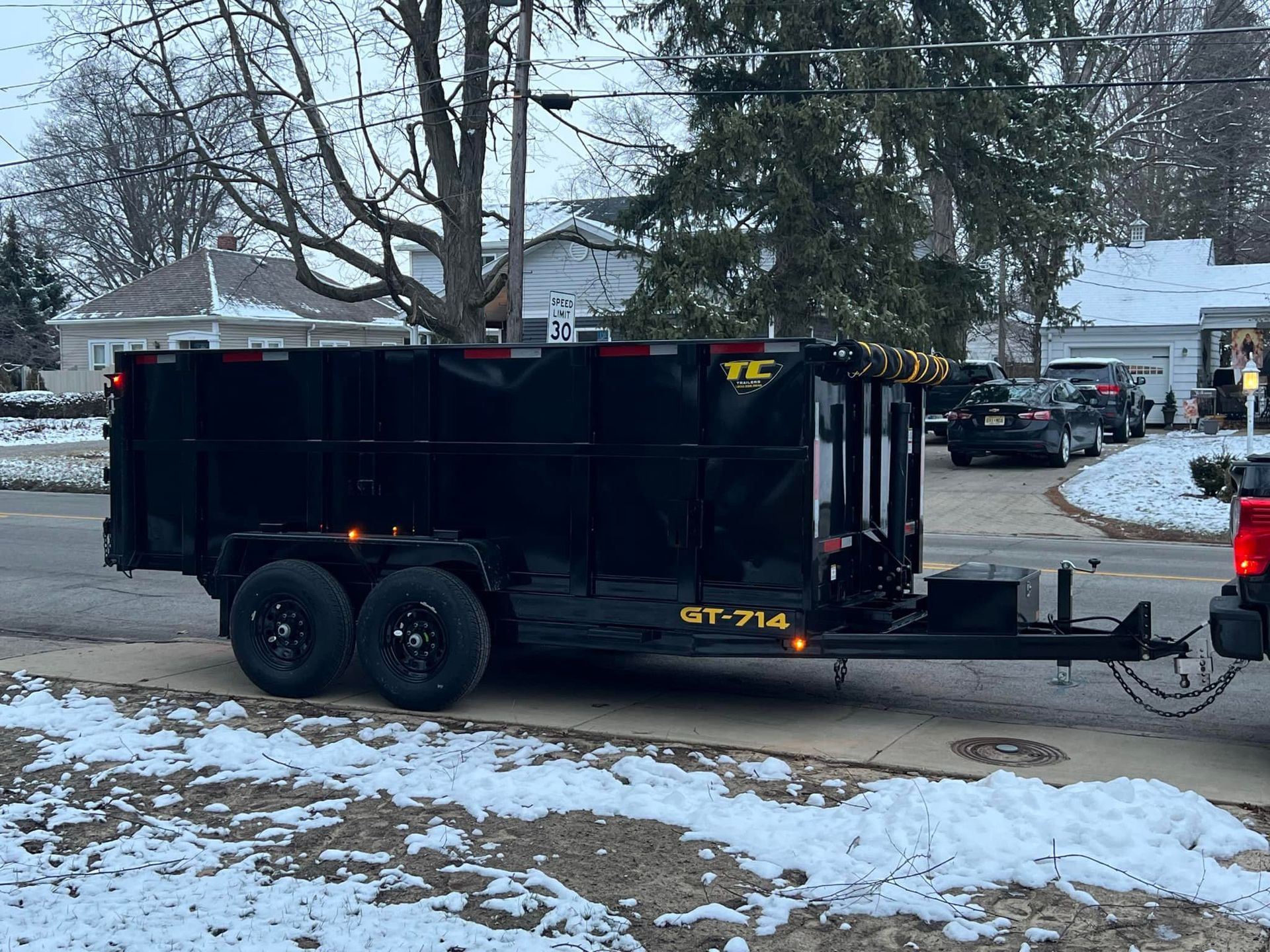 A dumpster trailer is parked on the side of the road in the snow.
