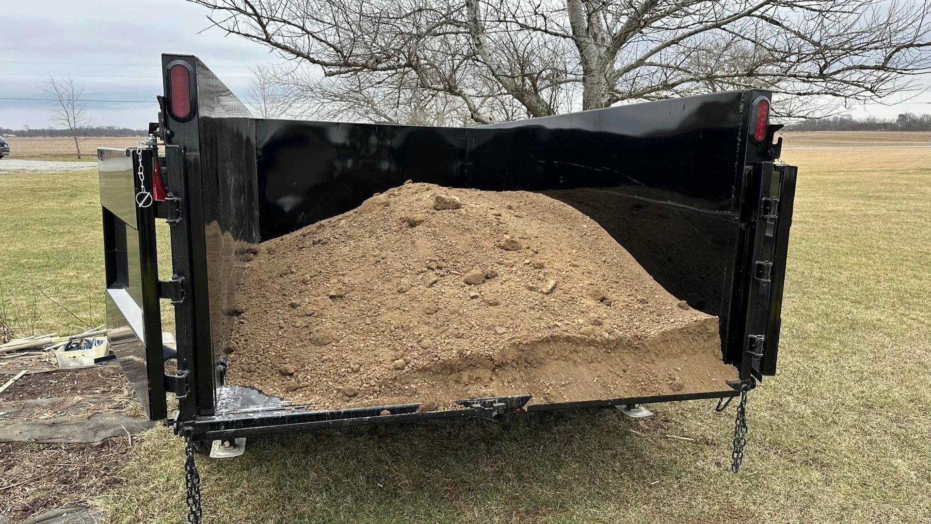 A dumpster filled with sand is parked in a grassy field.