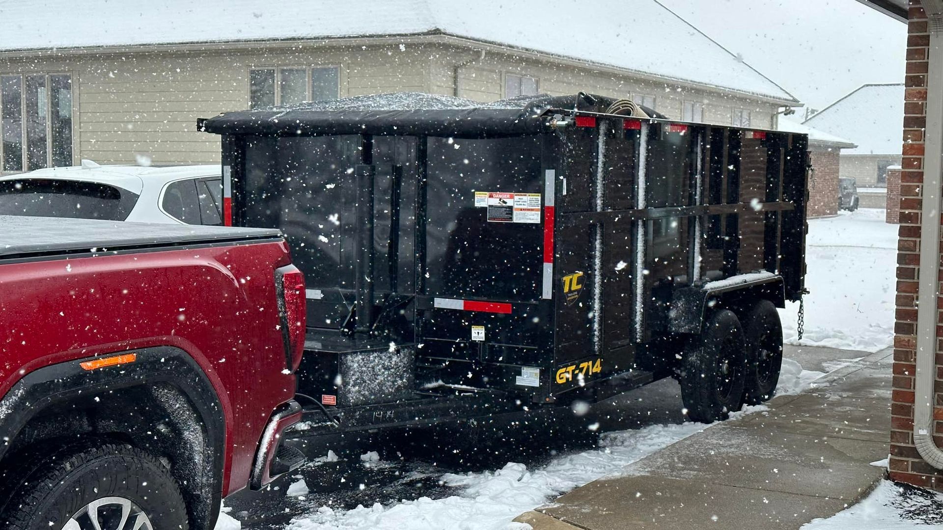 A red truck is parked next to a dumpster in the snow.