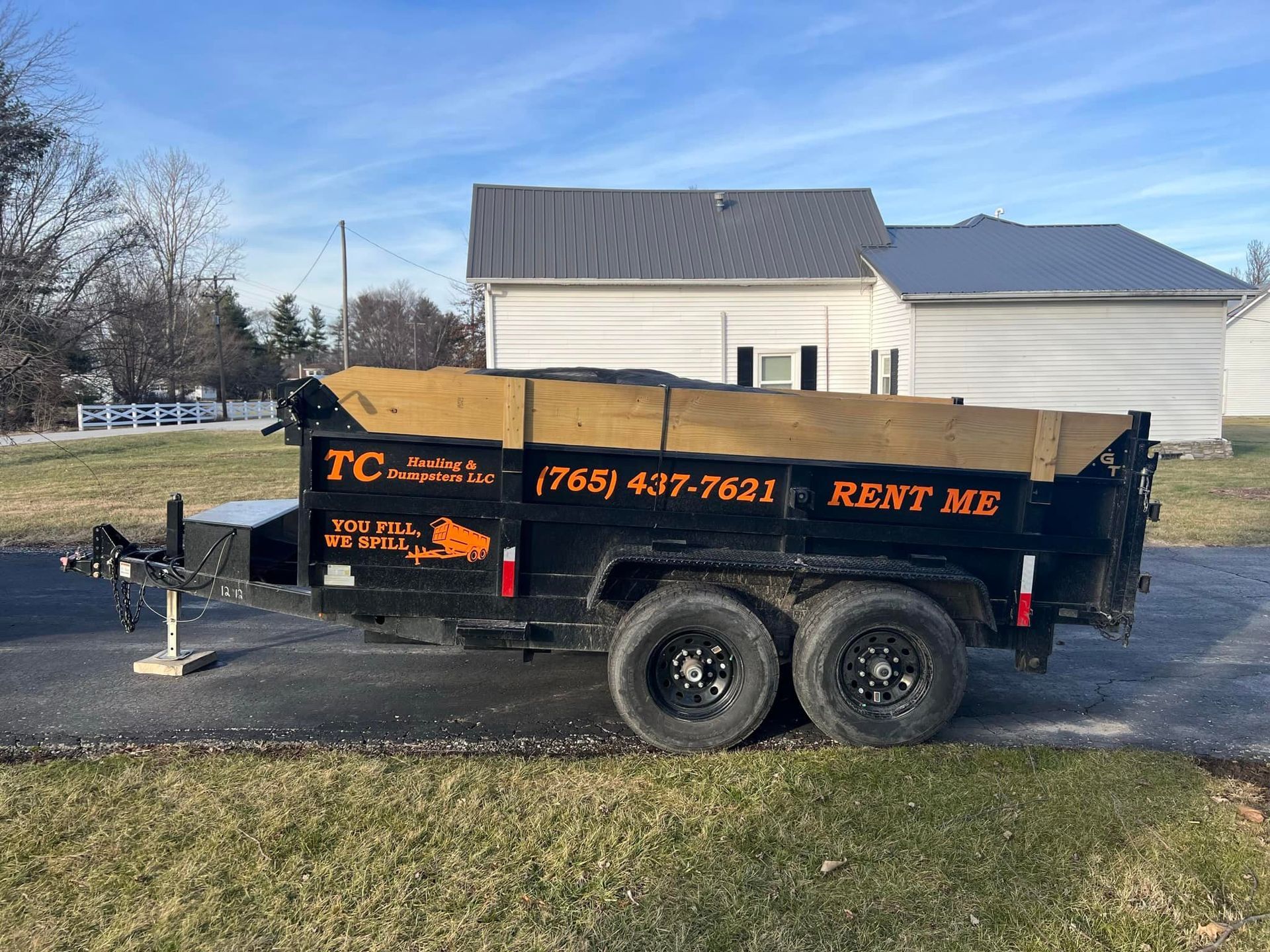 A dumpster is parked on the side of the road in front of a house.