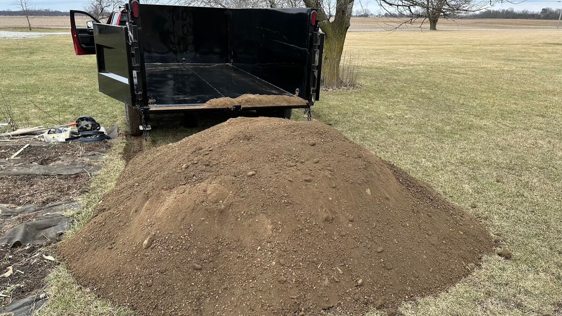A pile of dirt is sitting next to a trailer in a field.