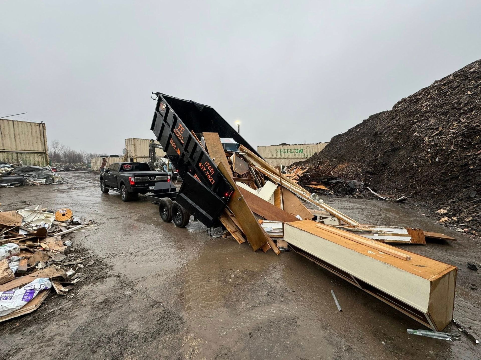 A dump truck is sitting on the side of the road next to a pile of trash.