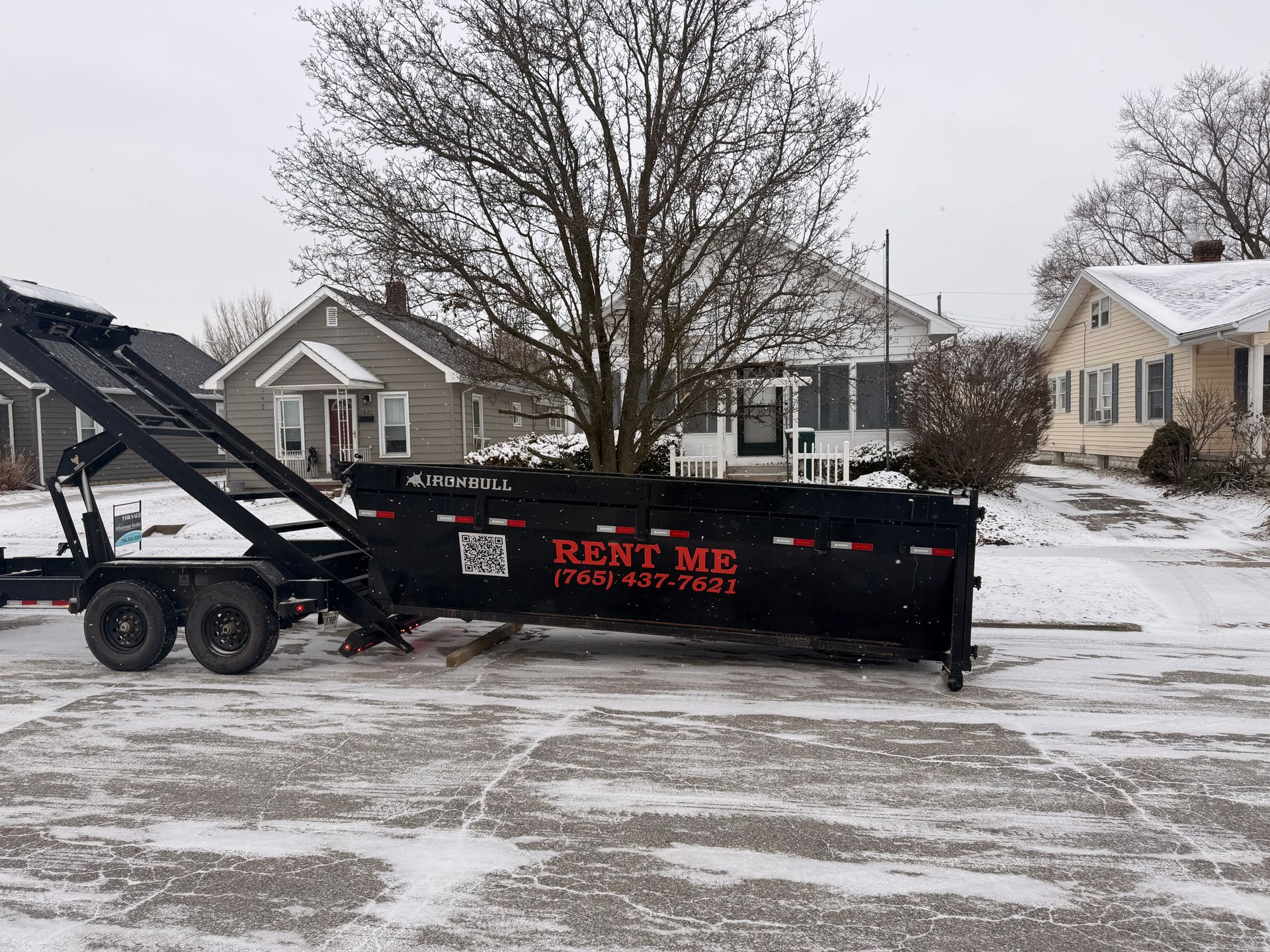 A dumpster trailer is parked in a driveway next to a truck.