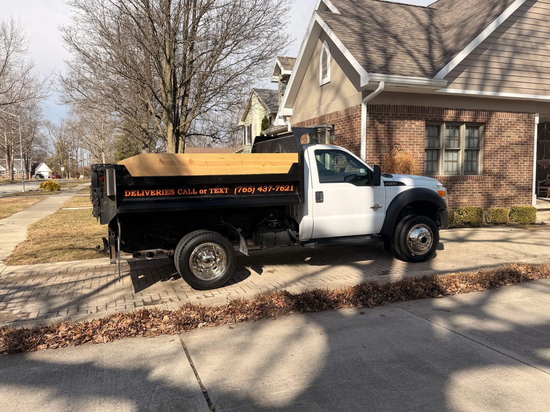 A white dump truck parked in the driveway of a brick suburban house on a sunny day.