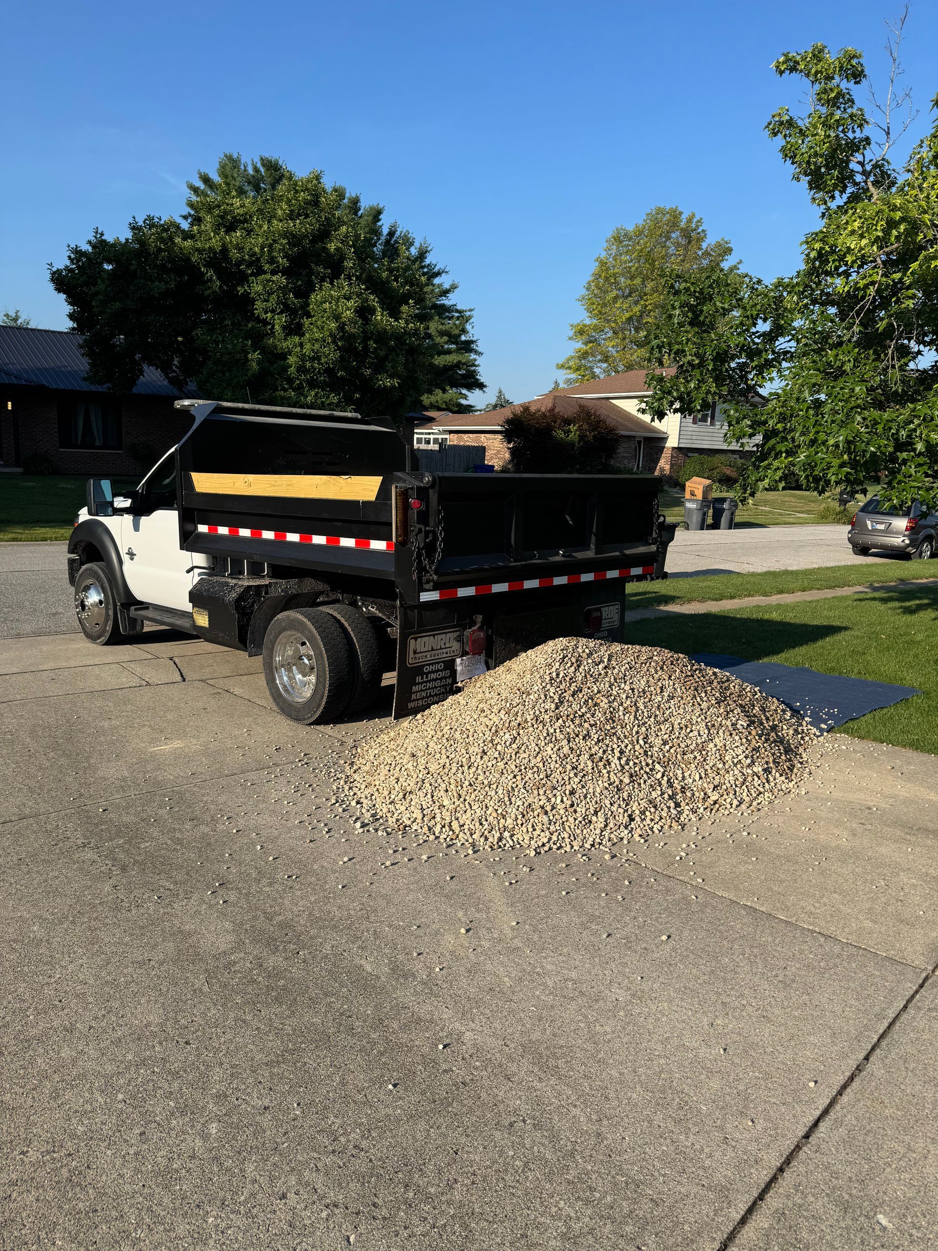 A white dump truck parked on a gravel driveway, emptying a large pile of light-colored stones onto the ground.