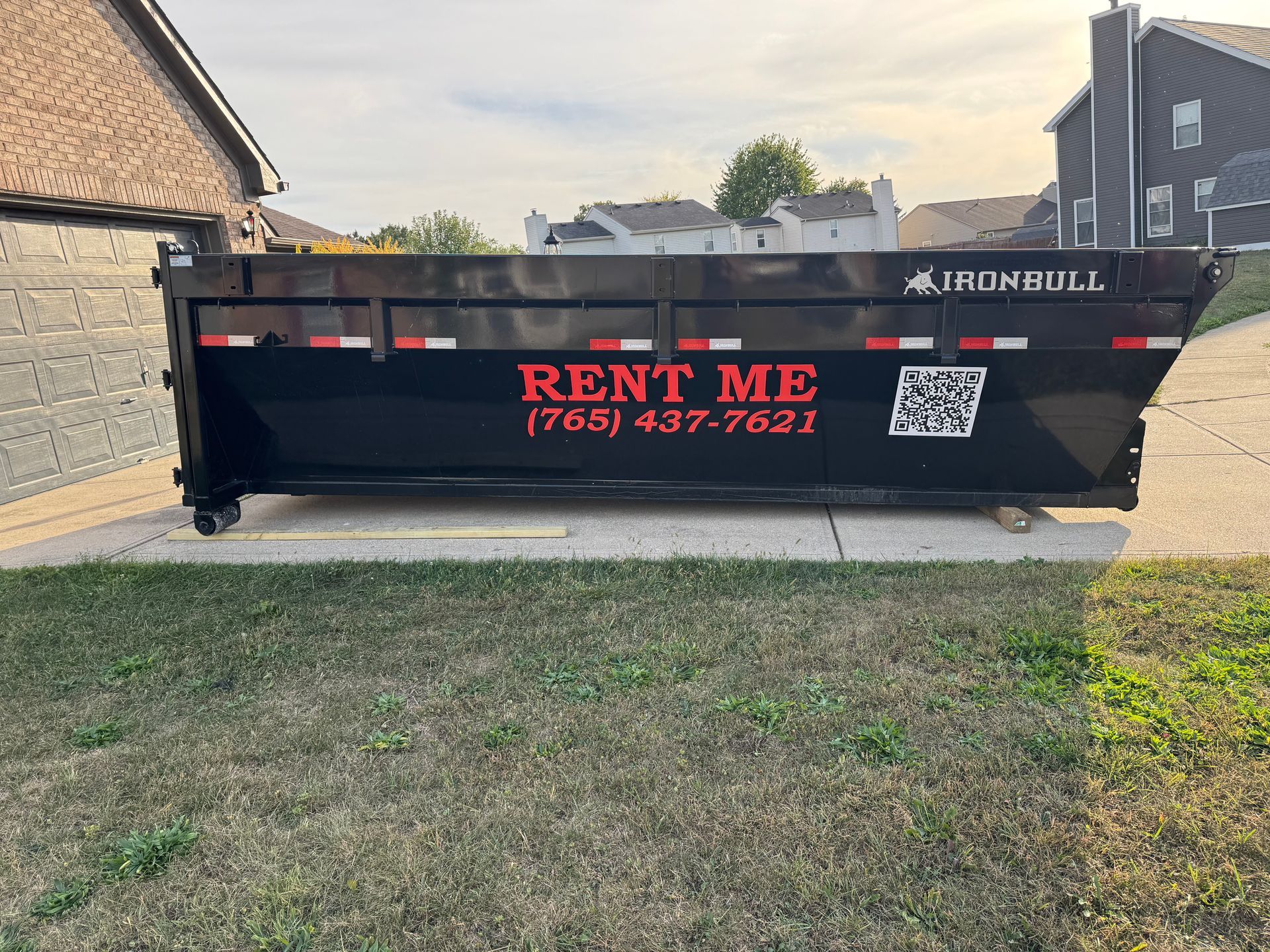 A black dumpster sits on a residential driveway, labeled with 