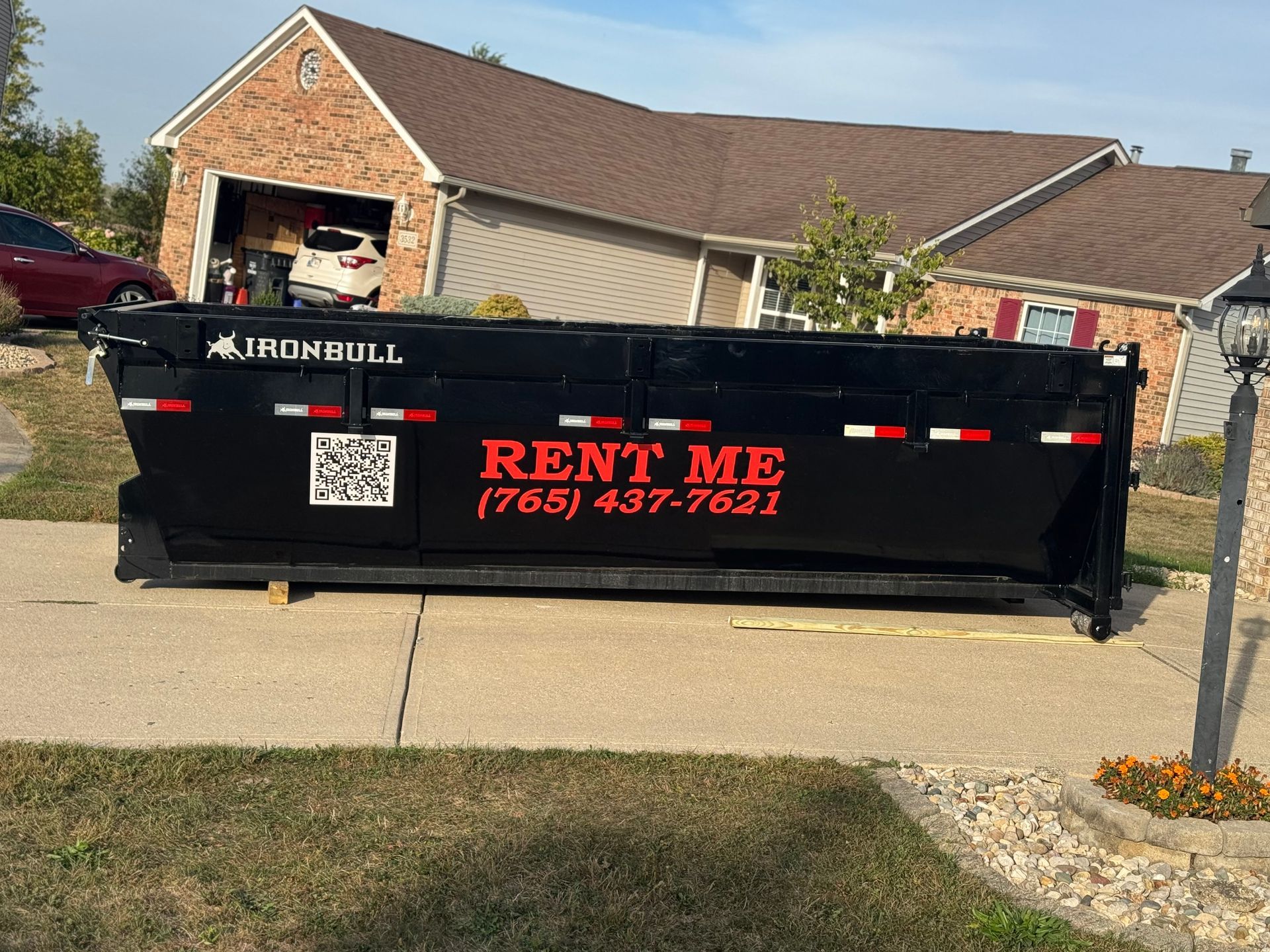 A black Iron Bull dumpster sits on a residential concrete driveway with 