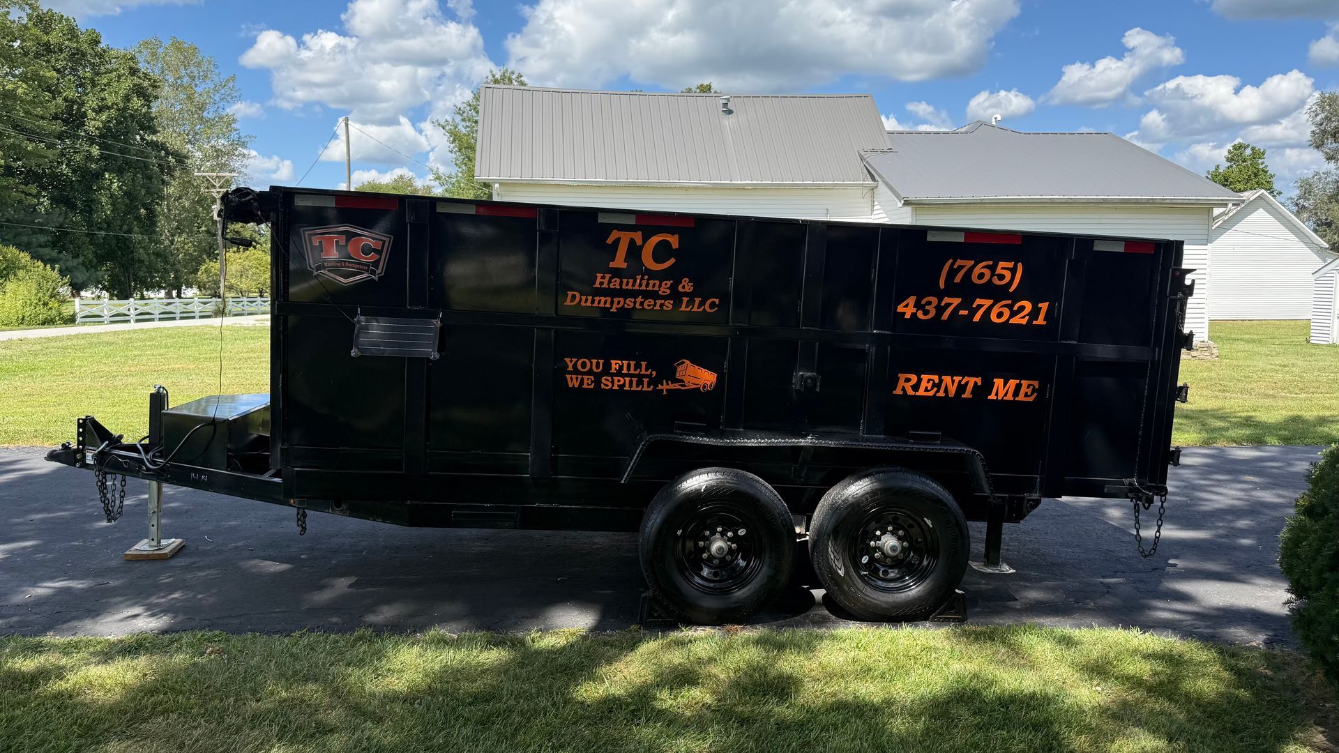 A black dumpster rental trailer parked on a driveway with bright orange text displaying company info and phone number.