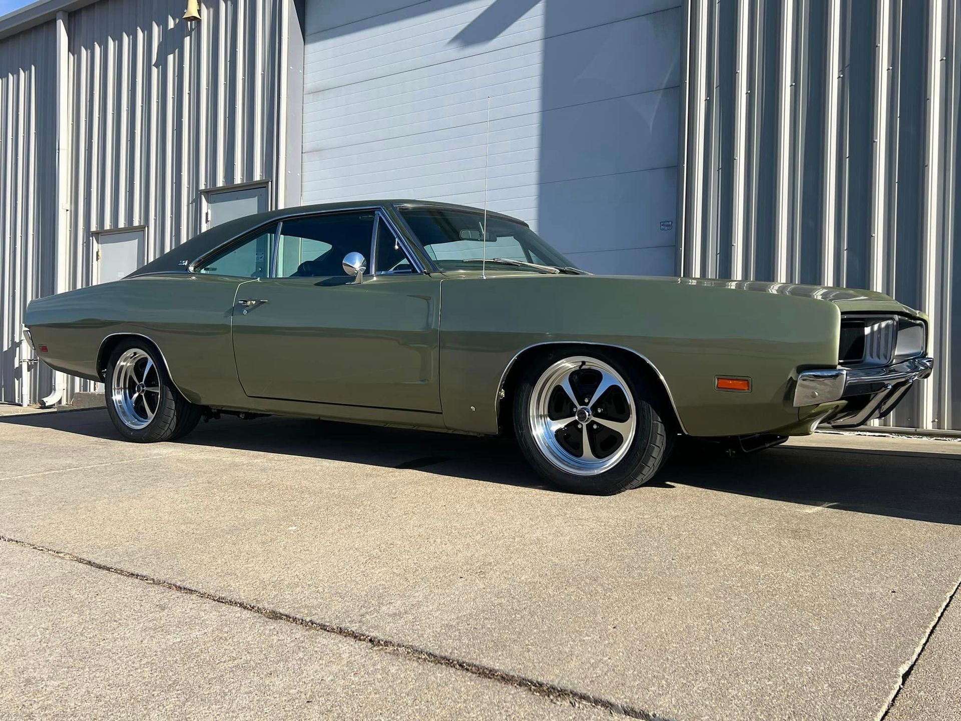 A green dodge charger is parked in front of a building.