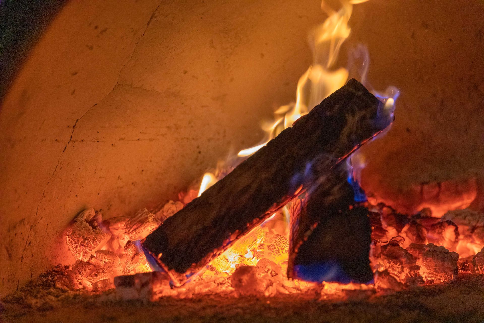 Logs burning in a fireplace, with bright orange flames and glowing embers.