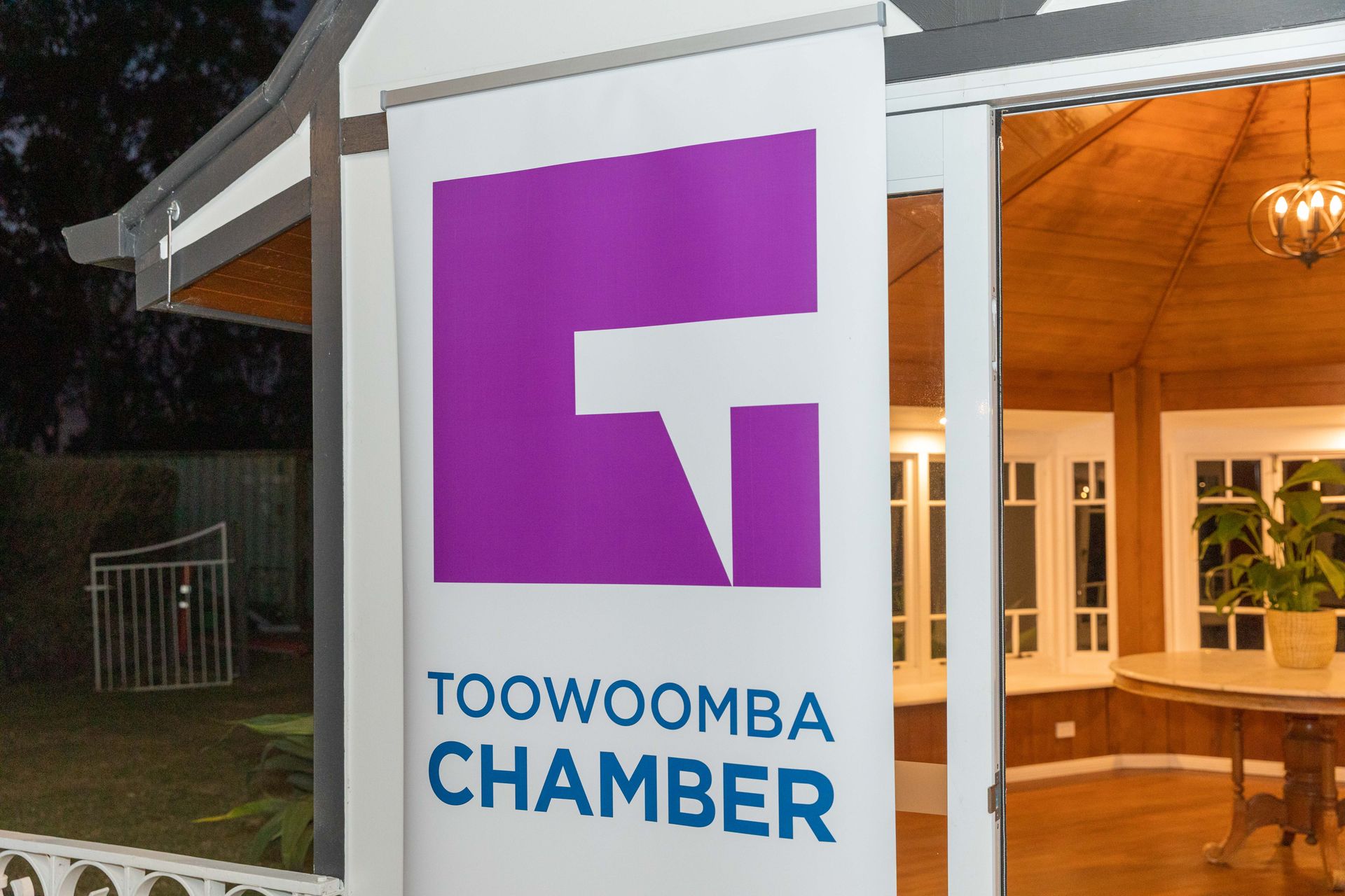A banner for Toowoomba Chamber featuring a purple and white logo. The sign hangs in front of a building at dusk.