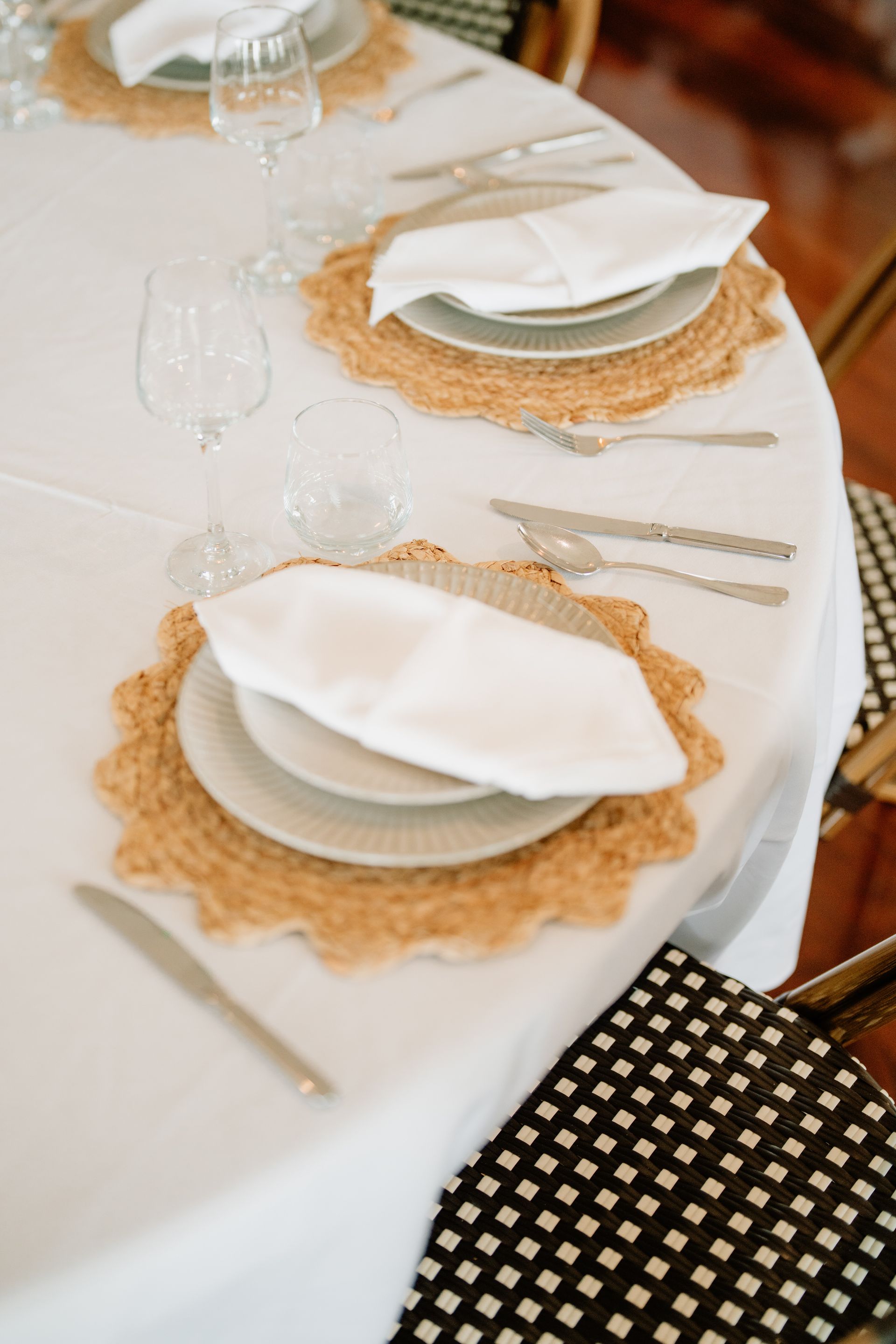 Bright, spacious interior with round tables set for dining. White tablecloths and chairs, wood floors, and large windows.