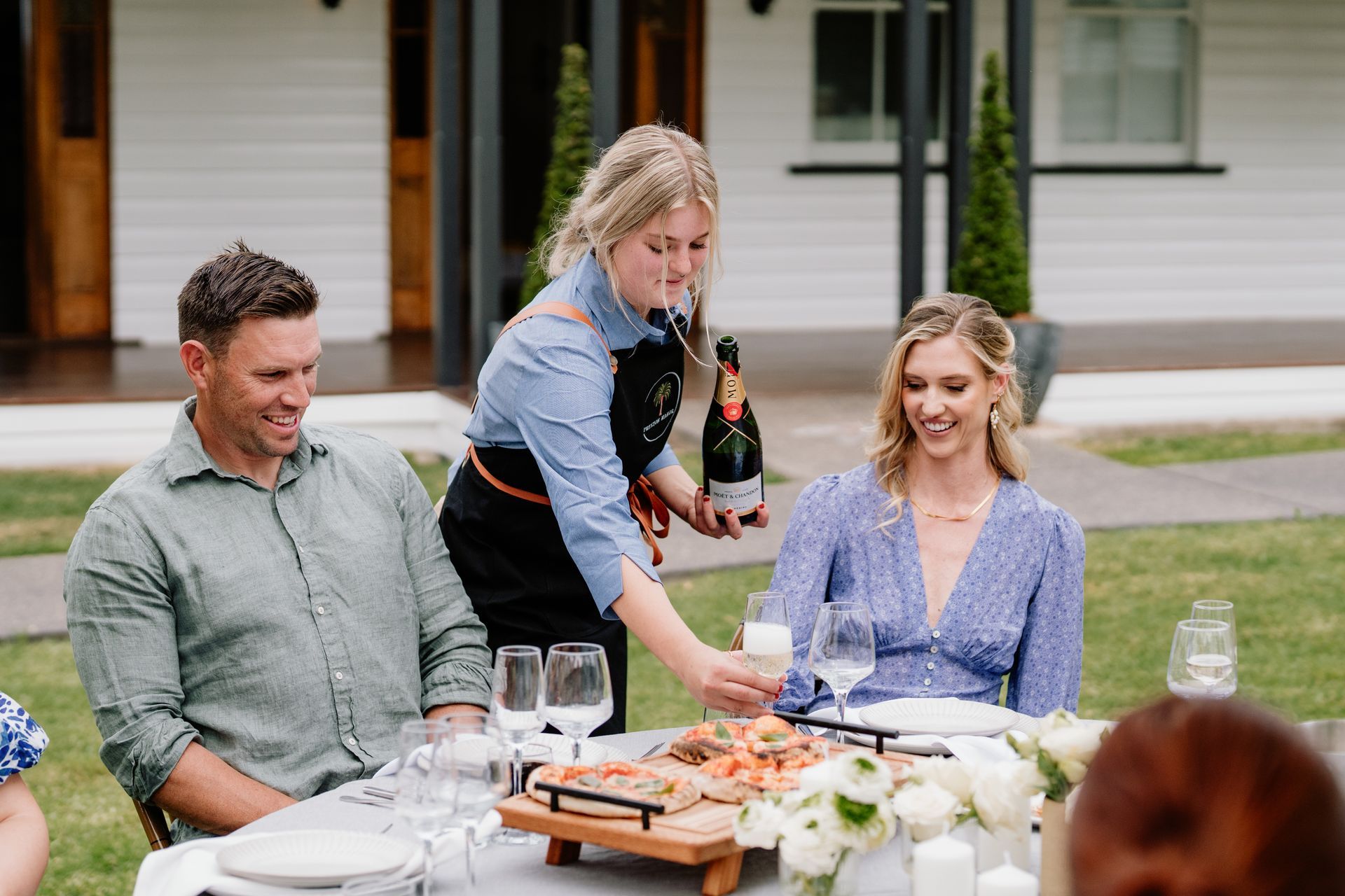 Lush green lawn and garden with a white building and a glass structure in the background, viewed through flowers.
