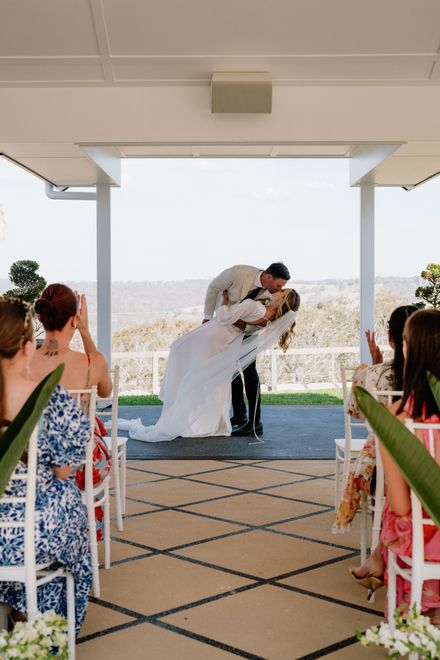 Wedding ceremony setup in a lavender field with a flower-covered altar and wooden benches facing a scenic valley at sunset.