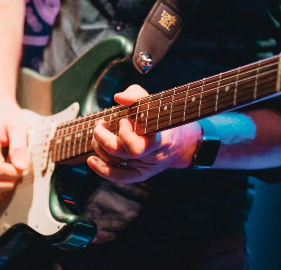 A person playing a green electric guitar, close up on their hands and the instrument.