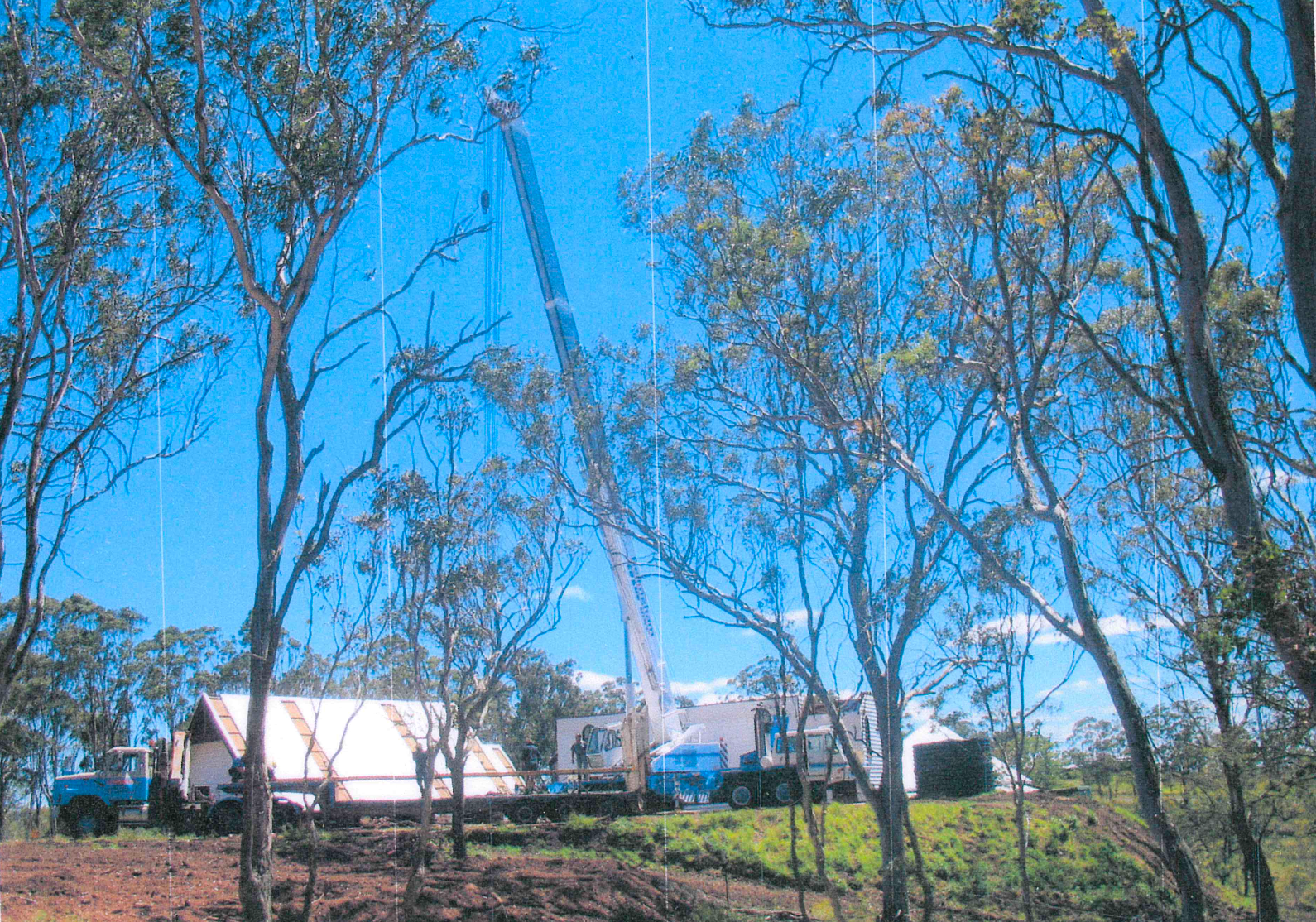 A crane operating in a wooded area; a truck and other equipment are set up on the ground.
