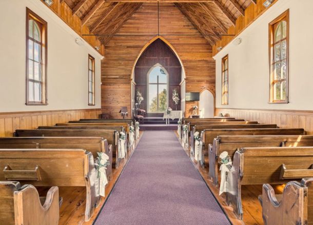 Inside of a wooden church, rows of pews face an altar with a large window. Sunlight streams in, illuminating the interior.