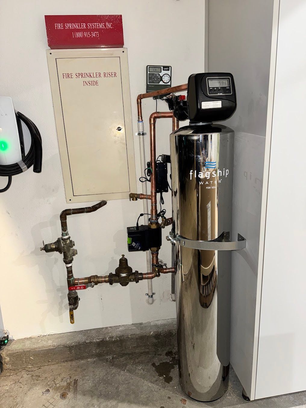 A stainless steel water filter is sitting in a corner of a room.