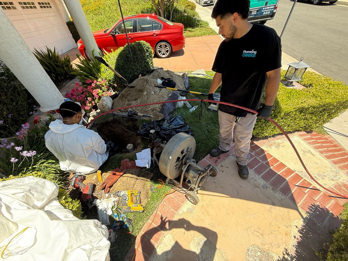 A man and a woman are working on a drain in a yard.